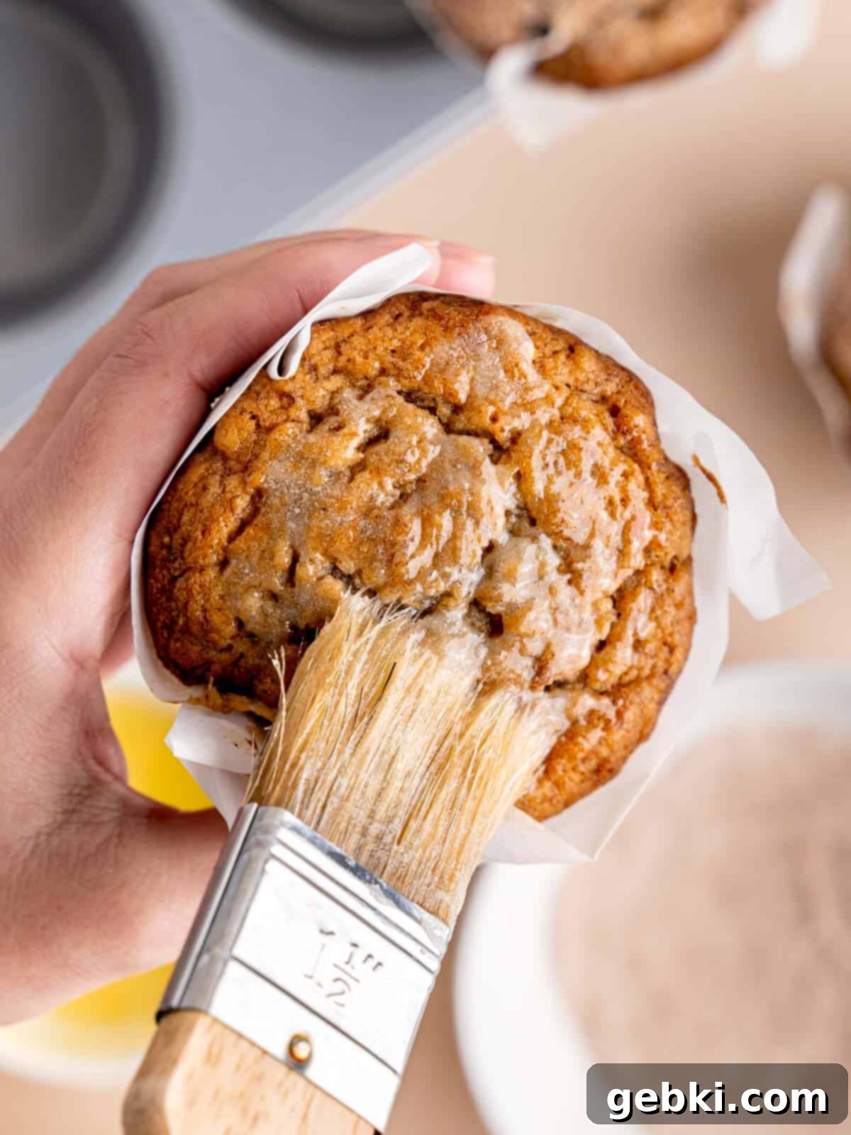 Cinnamon Swirl Banana Bread Muffins 8 Brushing melted butter on top of a cooled banana bread muffin, preparing it for the cinnamon sugar topping.