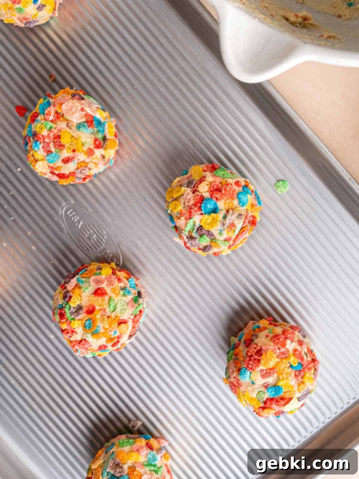 Cookie dough balls coated in Fruity Pebbles cereal on a baking sheet.
