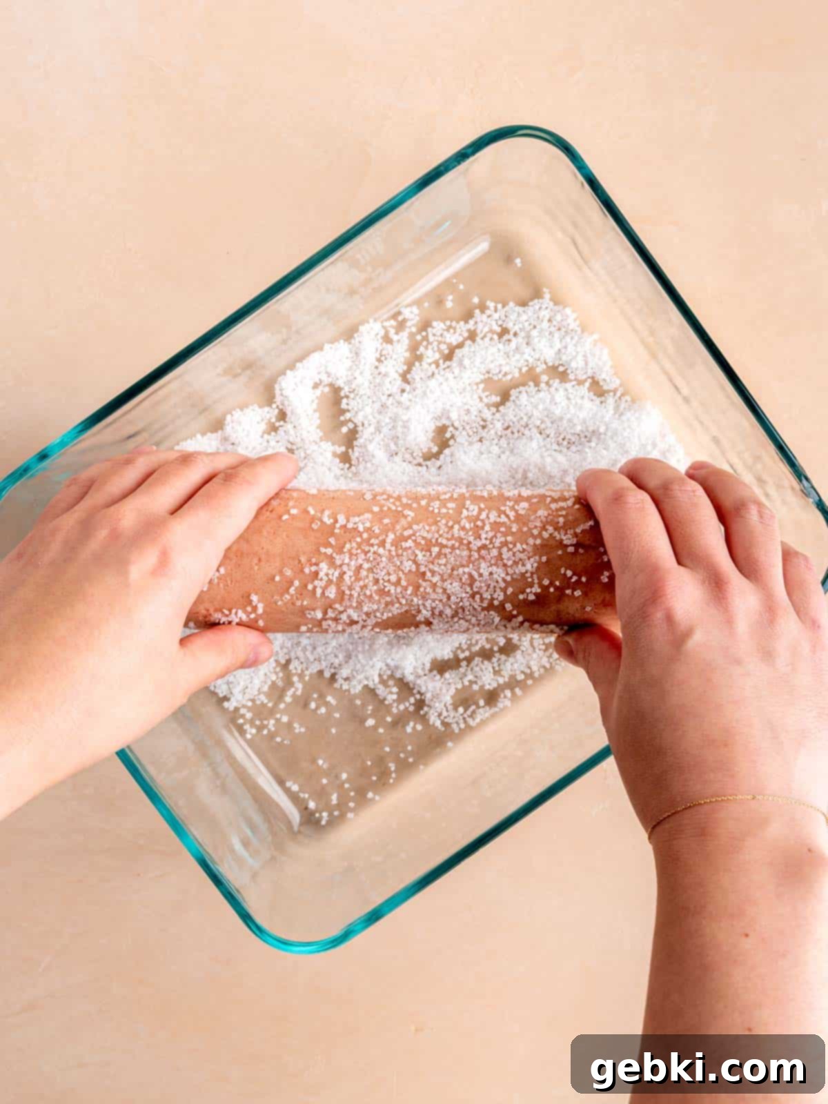 Effortless Strawberry Shortbread Cookies 7 Hands rolling a log of strawberry shortbread cookie dough in sparkling sugar, creating a glistening crust.