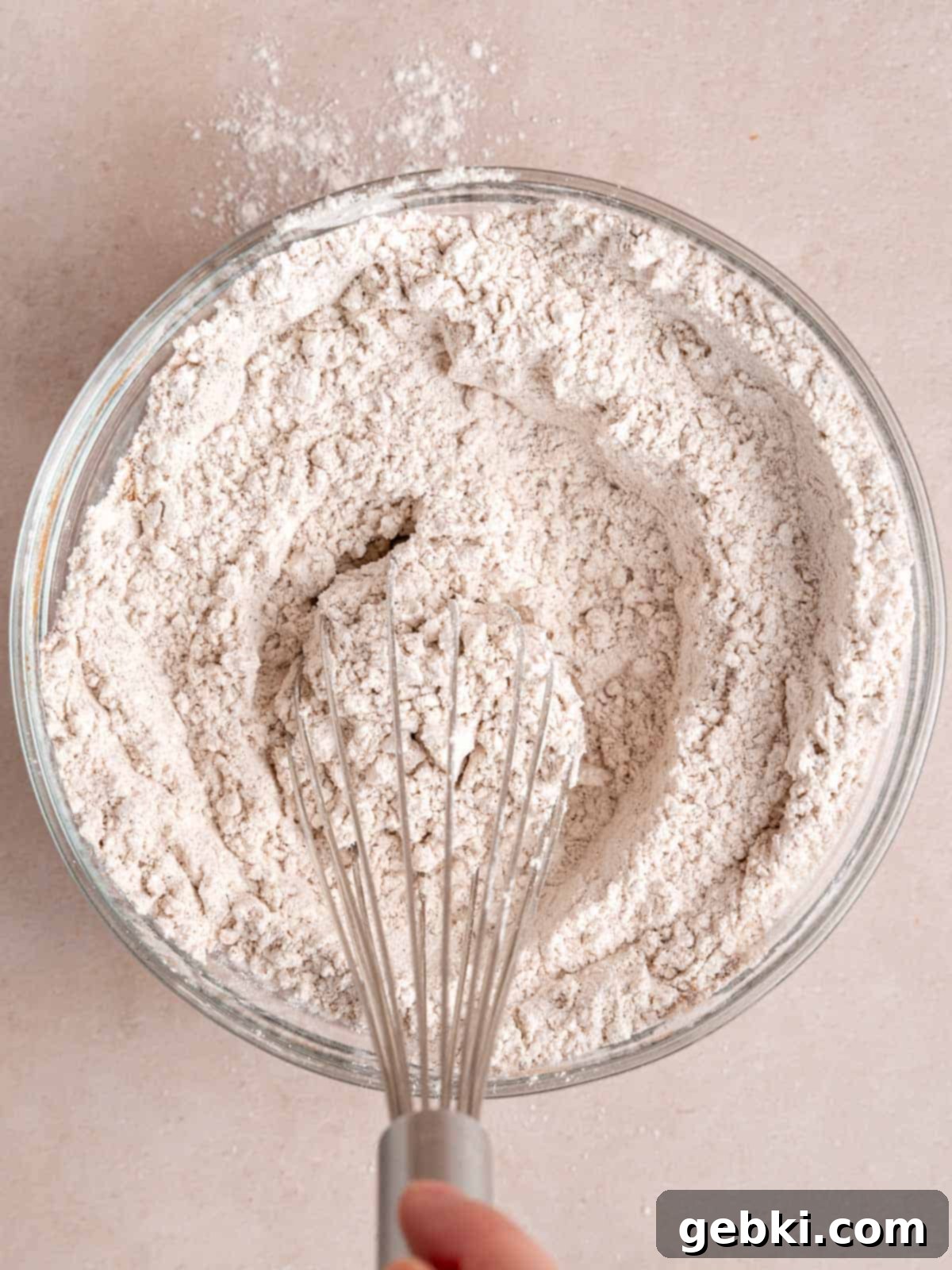 Whisking together dry ingredients like flour and spices for carrot cake in a mixing bowl.