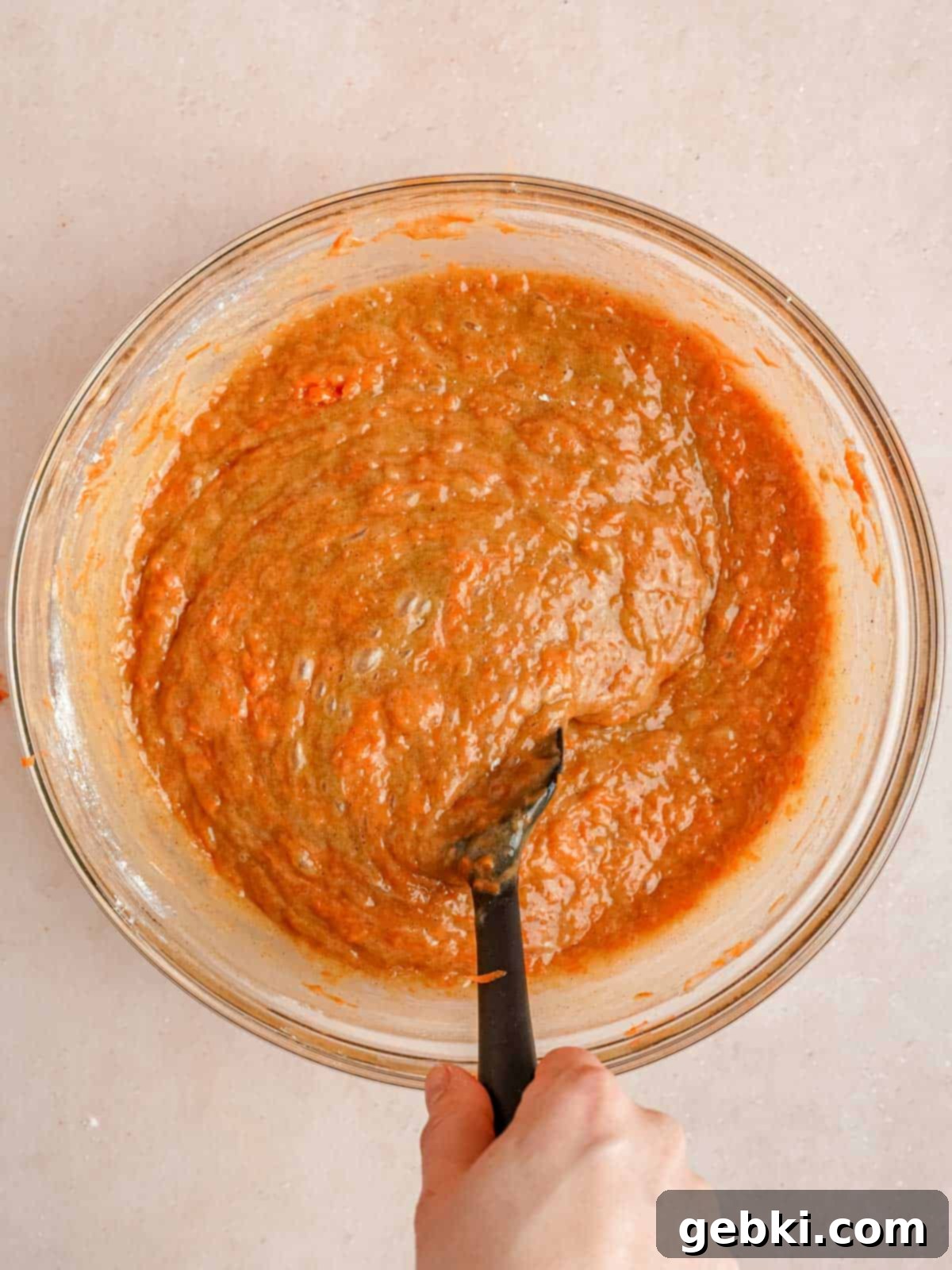 Folding freshly grated carrots into a spiced cake batter, showing the rich color.