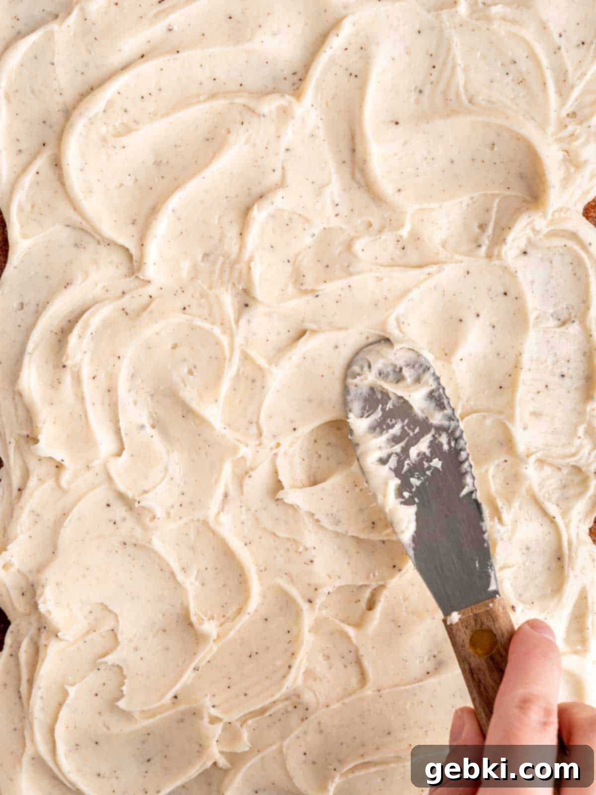 Spreading smooth brown butter cream cheese frosting evenly over a cooled spiced carrot sheet cake.