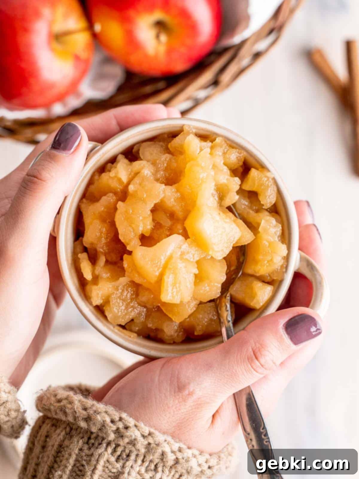 Rustic Apple Chunks 2 Hands gently holding a bowl of warm, homemade chunky applesauce, highlighting its rustic texture and inviting aroma.