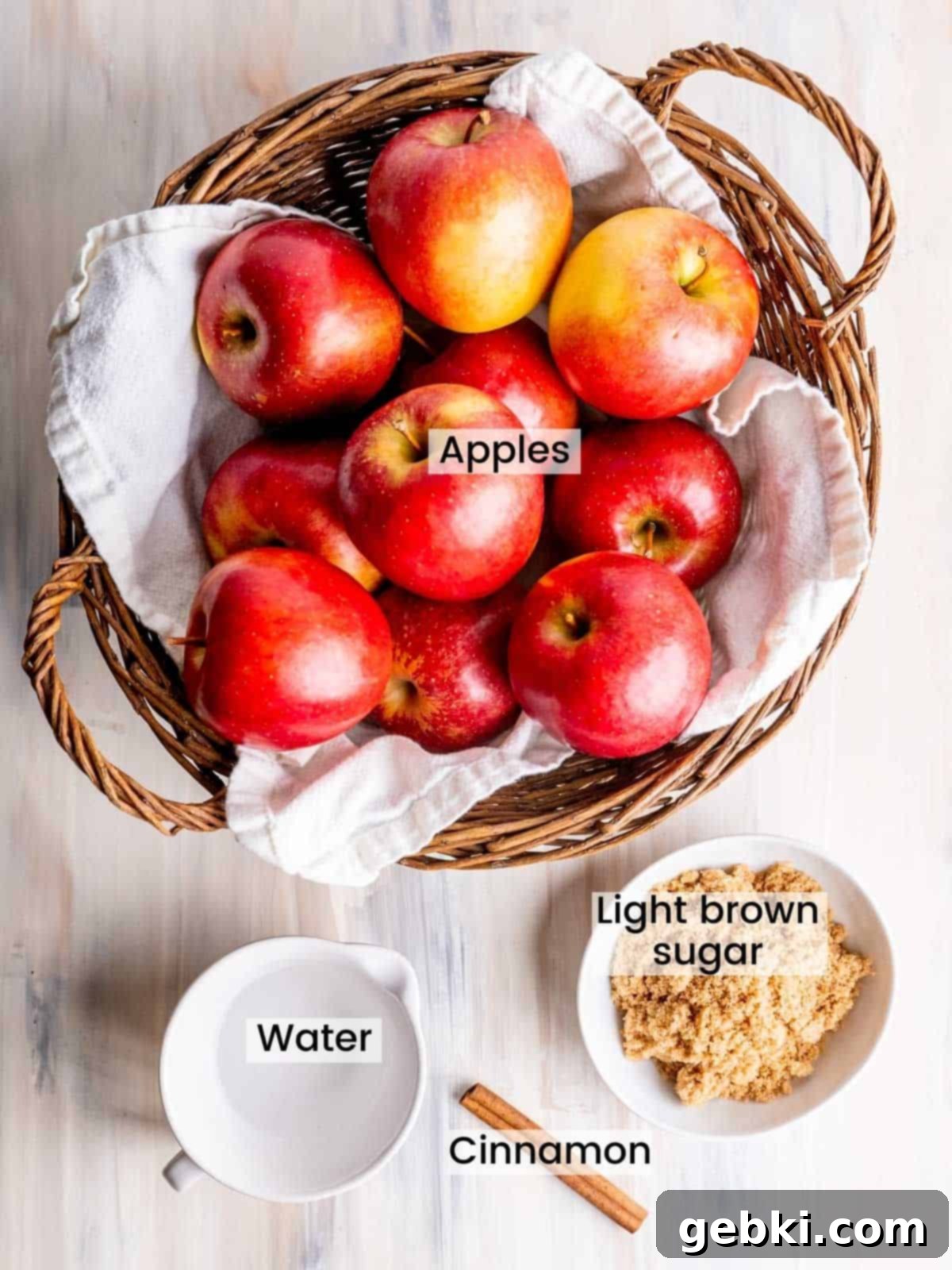 Rustic Apple Chunks 3 Labeled ingredients for homemade chunky applesauce: a pile of fresh apples, a bowl of light brown sugar, cinnamon sticks, and a small glass of water.