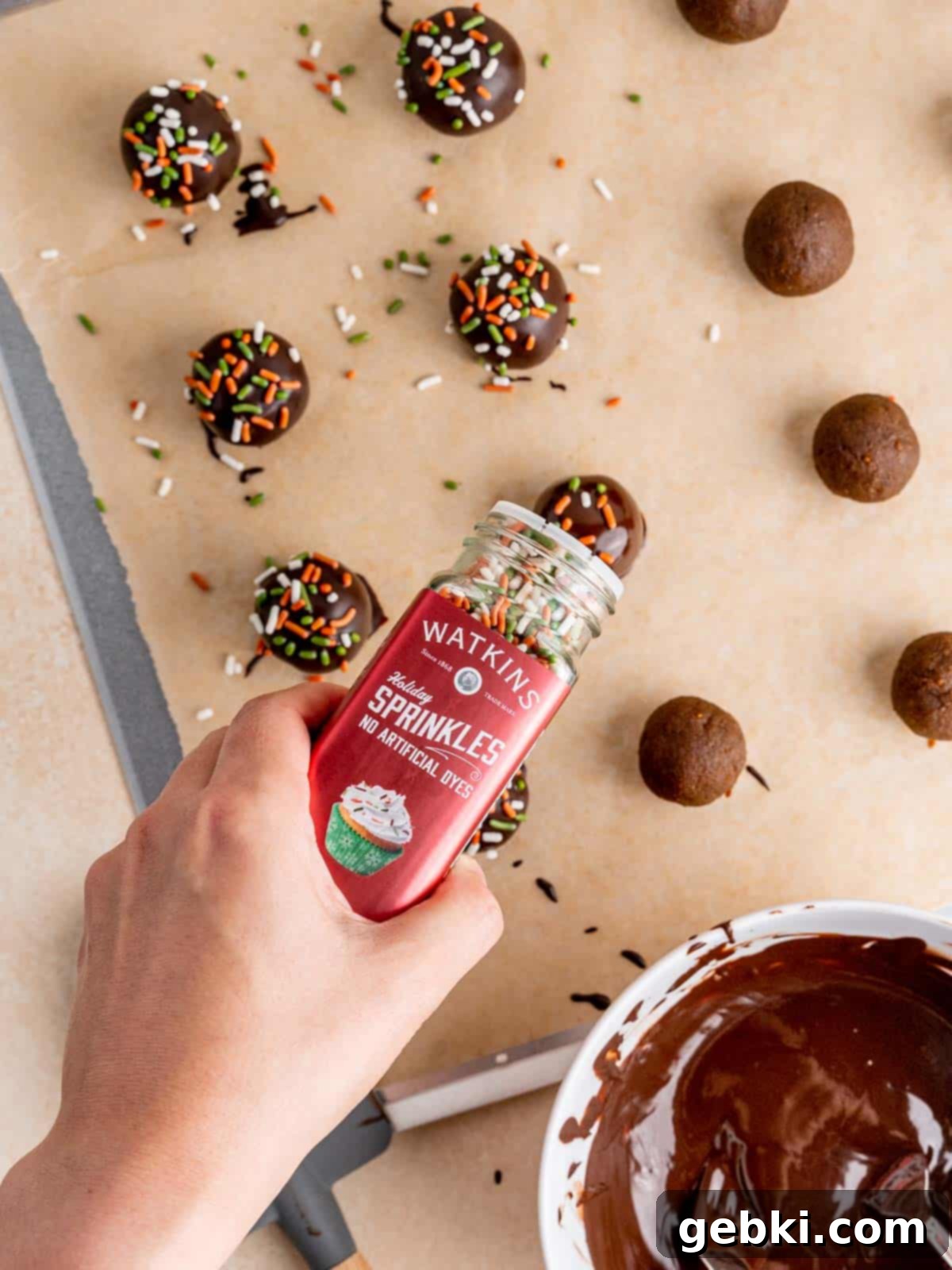 No-Bake Christmas Cookie Truffles 12 A rich chocolate-coated gingerbread cookie truffle being generously adorned with colorful Watkins Holiday sprinkles, creating a festive appearance.
