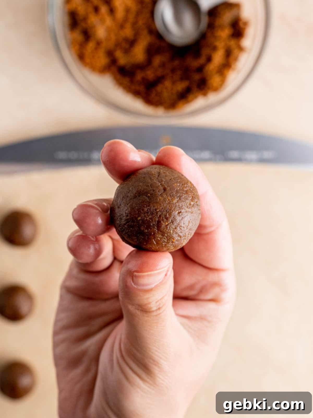 No-Bake Christmas Cookie Truffles 8 A hand gently holds a perfectly formed gingerbread truffle ball, showcasing its smooth texture before coating.