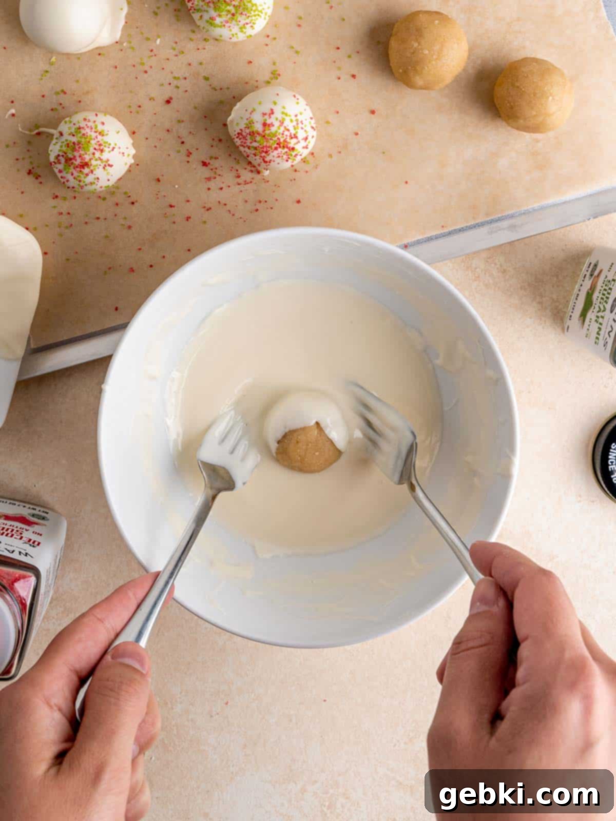 No-Bake Christmas Cookie Truffles 9 A sugar cookie truffle being carefully coated in a smooth, melted white chocolate mixture using a fork, ready for its festive decoration.