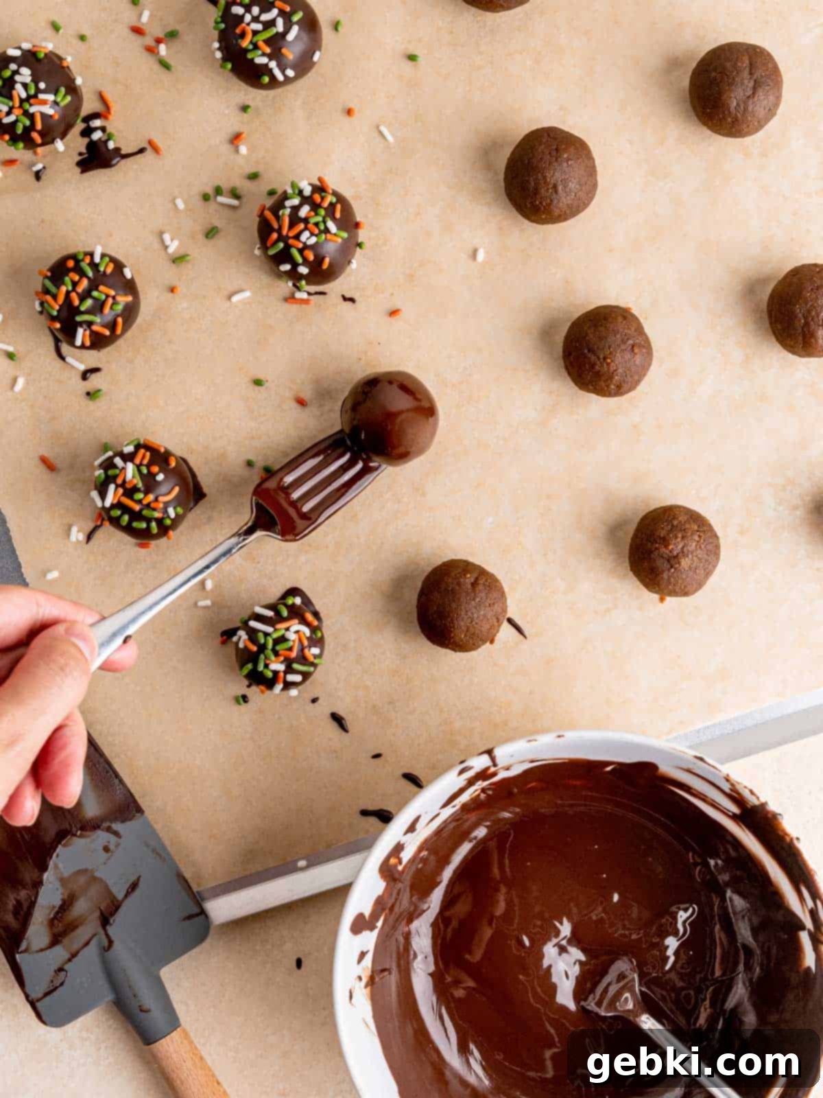 No-Bake Christmas Cookie Truffles 10 A freshly chocolate-covered gingerbread cookie truffle being gently placed onto a baking sheet, ready for quick topping with holiday sprinkles.