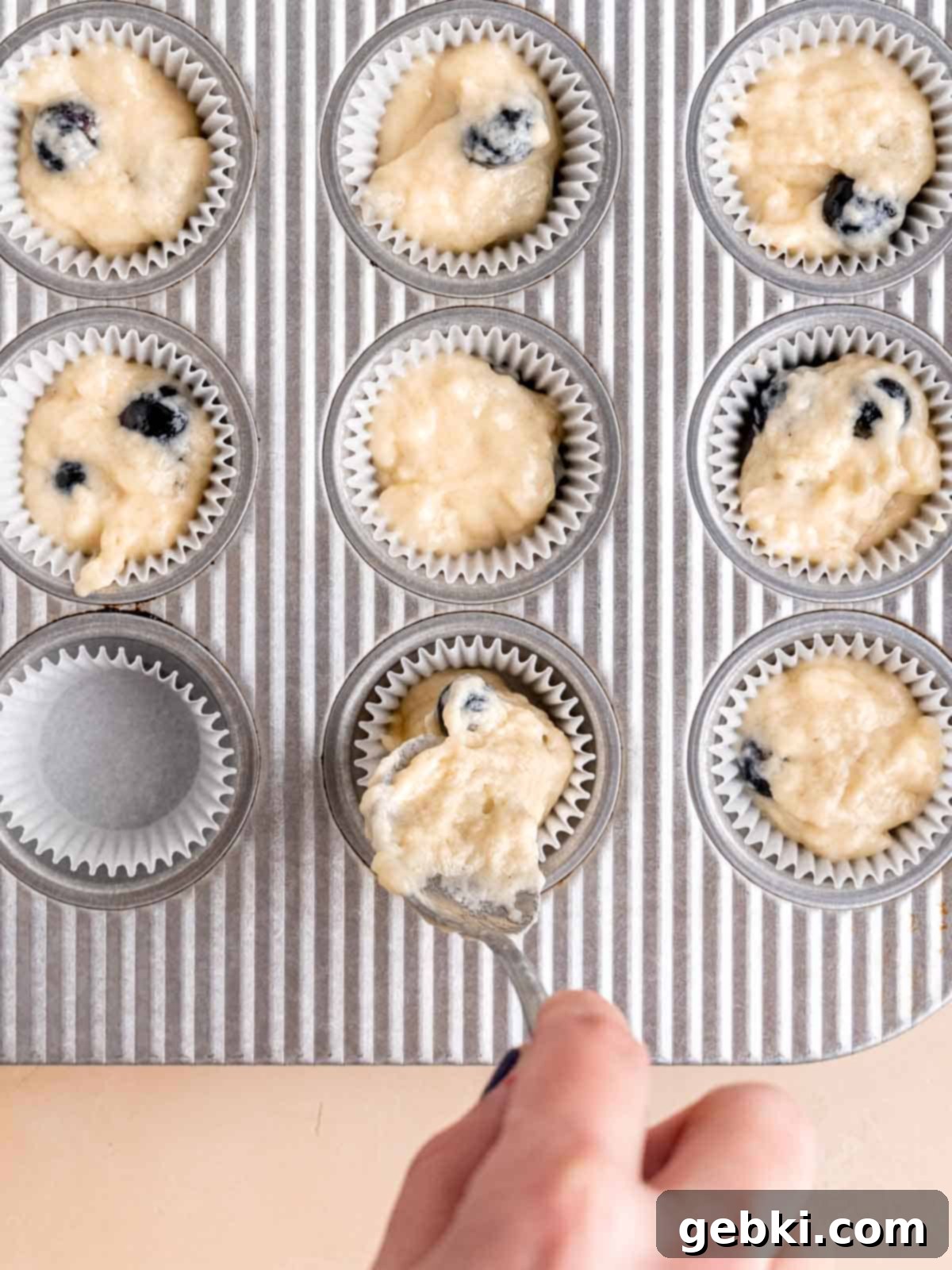Bite-Sized Blueberry Bliss 7 Spooning blueberry muffin batter into a mini muffin pan lined with paper cups.