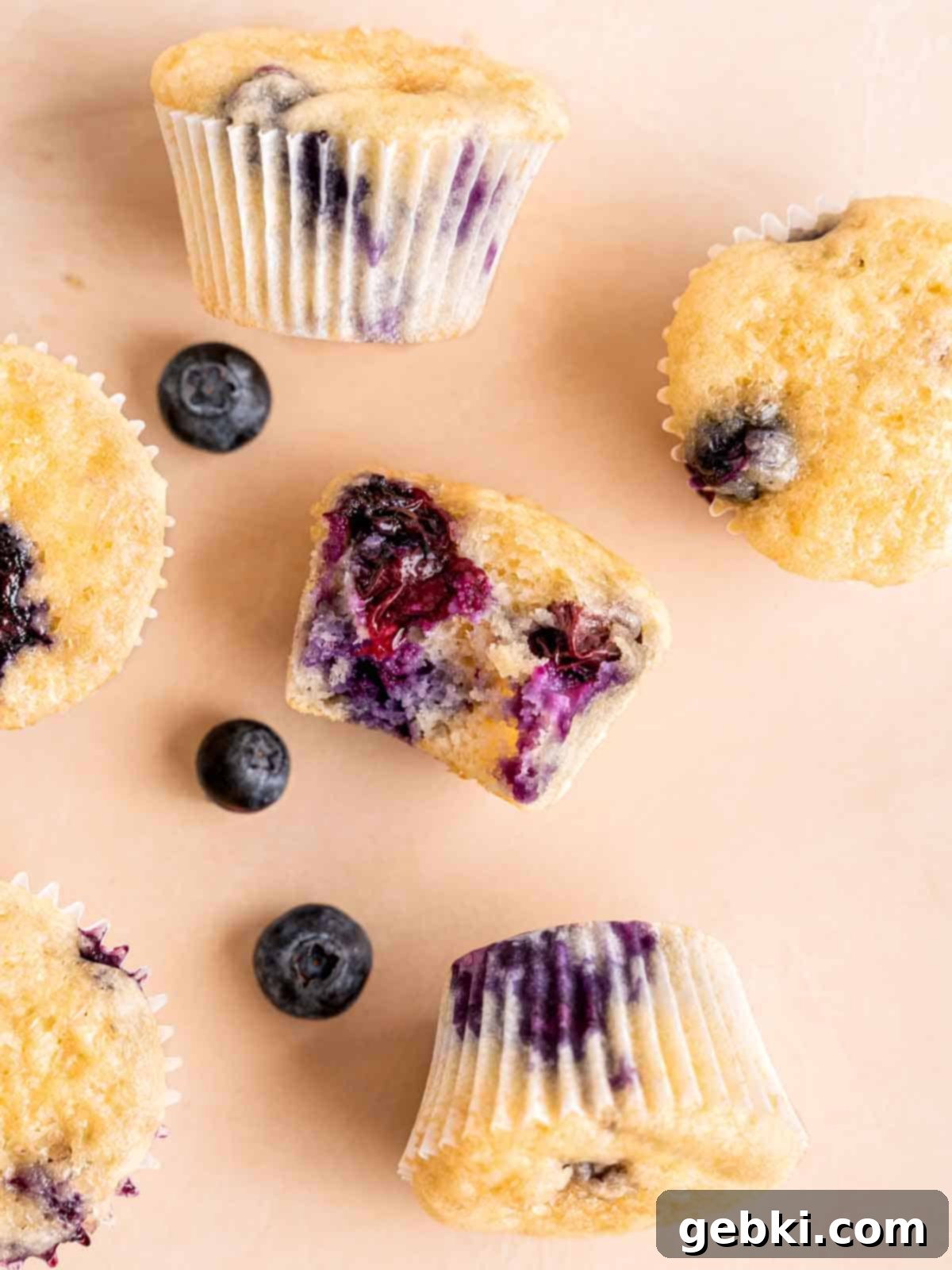 Bite-Sized Blueberry Bliss 8 Close-up of baked mini blueberry muffins resting next to fresh blueberries on a surface.