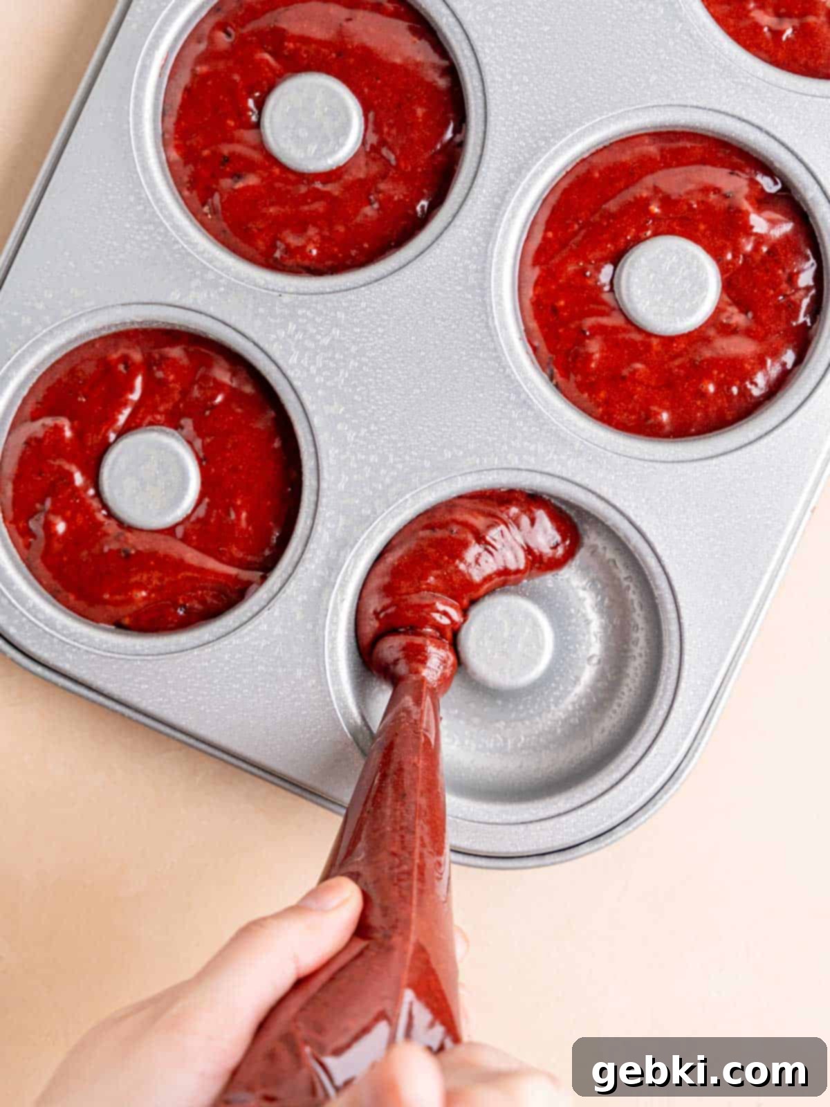 Frosted Red Velvet Donut Indulgence 7 Piping red velvet donut batter into a donut pan.