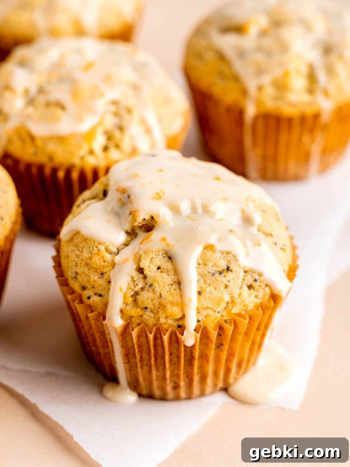 Zesty Orange Poppy Seed Muffins with Glaze 2 Jumbo orange poppy seed muffins with vanilla orange glaze, stacked on a cooling rack.