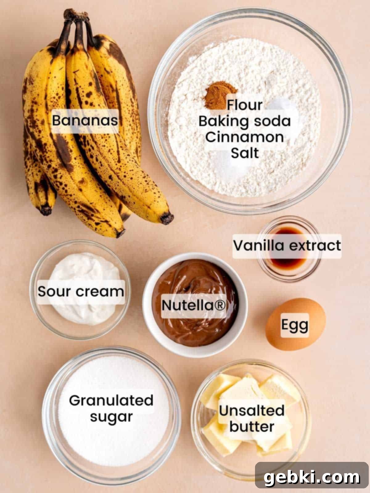 Marbleized Banana Nutella Muffins 3 A beautifully arranged collection of fresh, high-quality ingredients laid out on a clean surface, essential for making delicious Banana Nutella Muffins. This includes perfectly ripe bananas, creamy unsalted butter, granulated sugar, all-purpose flour, fragrant cinnamon, and a jar of iconic Nutella chocolate hazelnut spread.