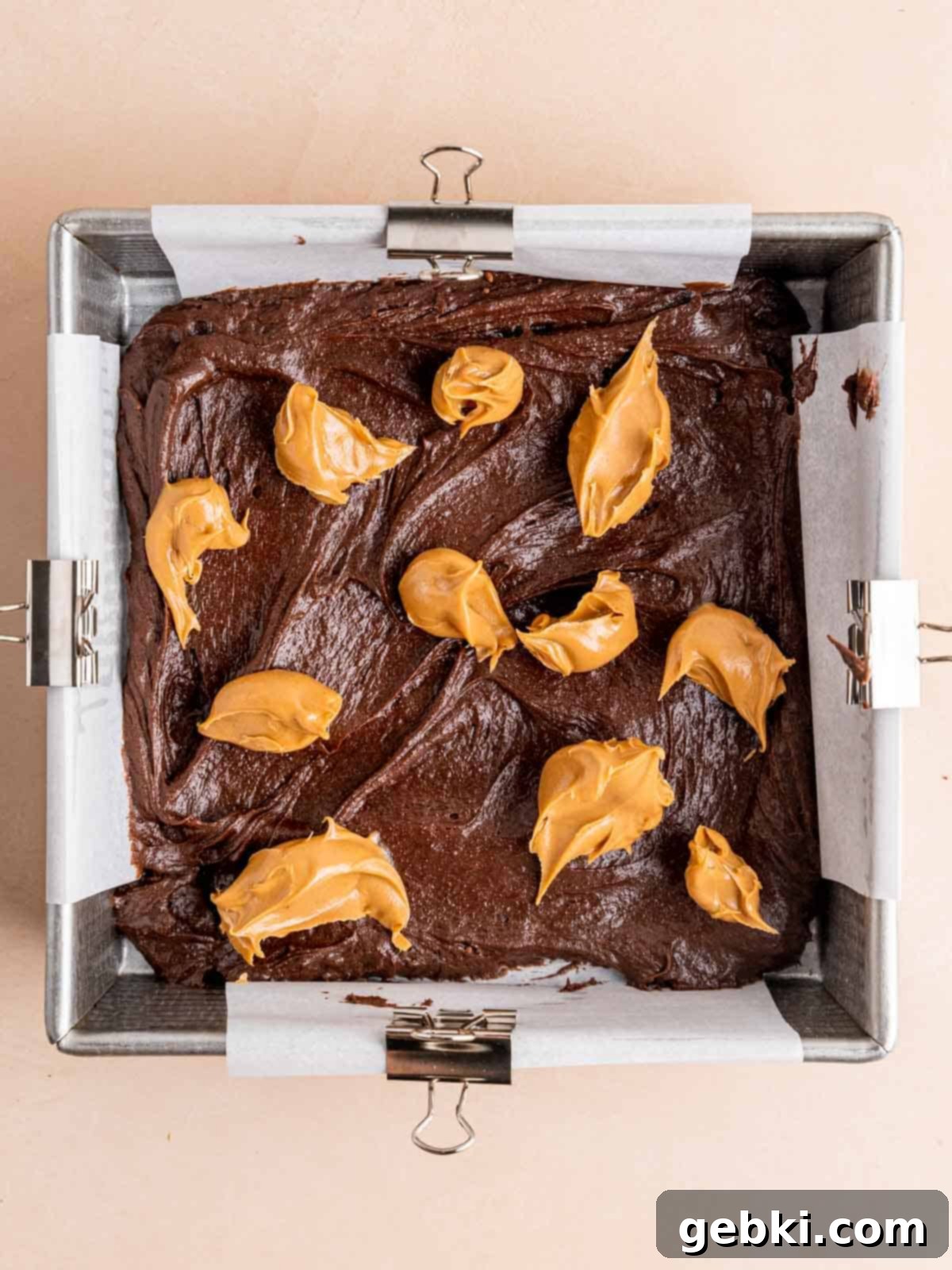 First layer of chocolate brownie batter in an 8x8 inch pan, topped with dollops of creamy peanut butter.