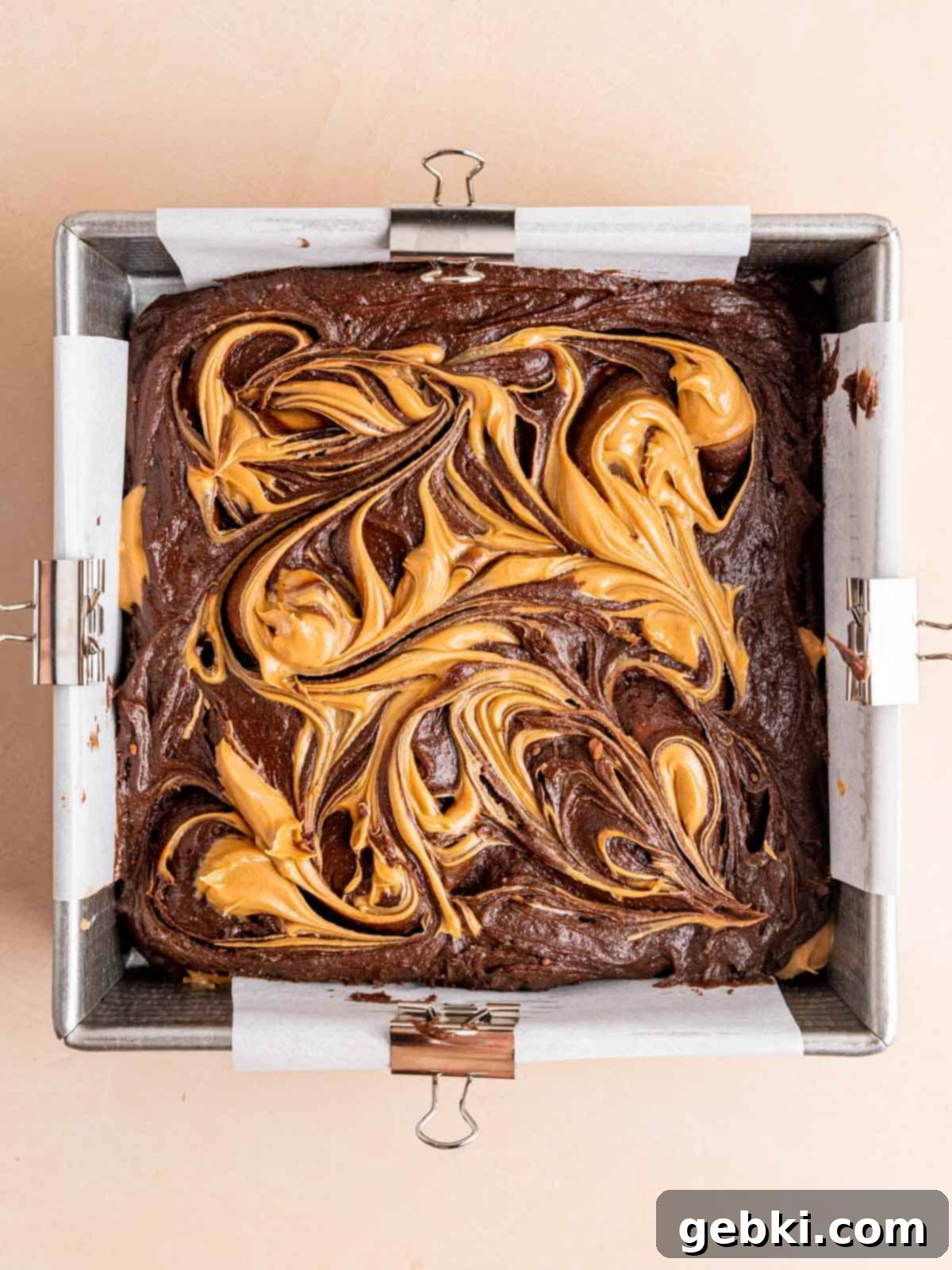 Beautifully swirled peanut butter on top of the chocolate brownie batter in a square baking pan.