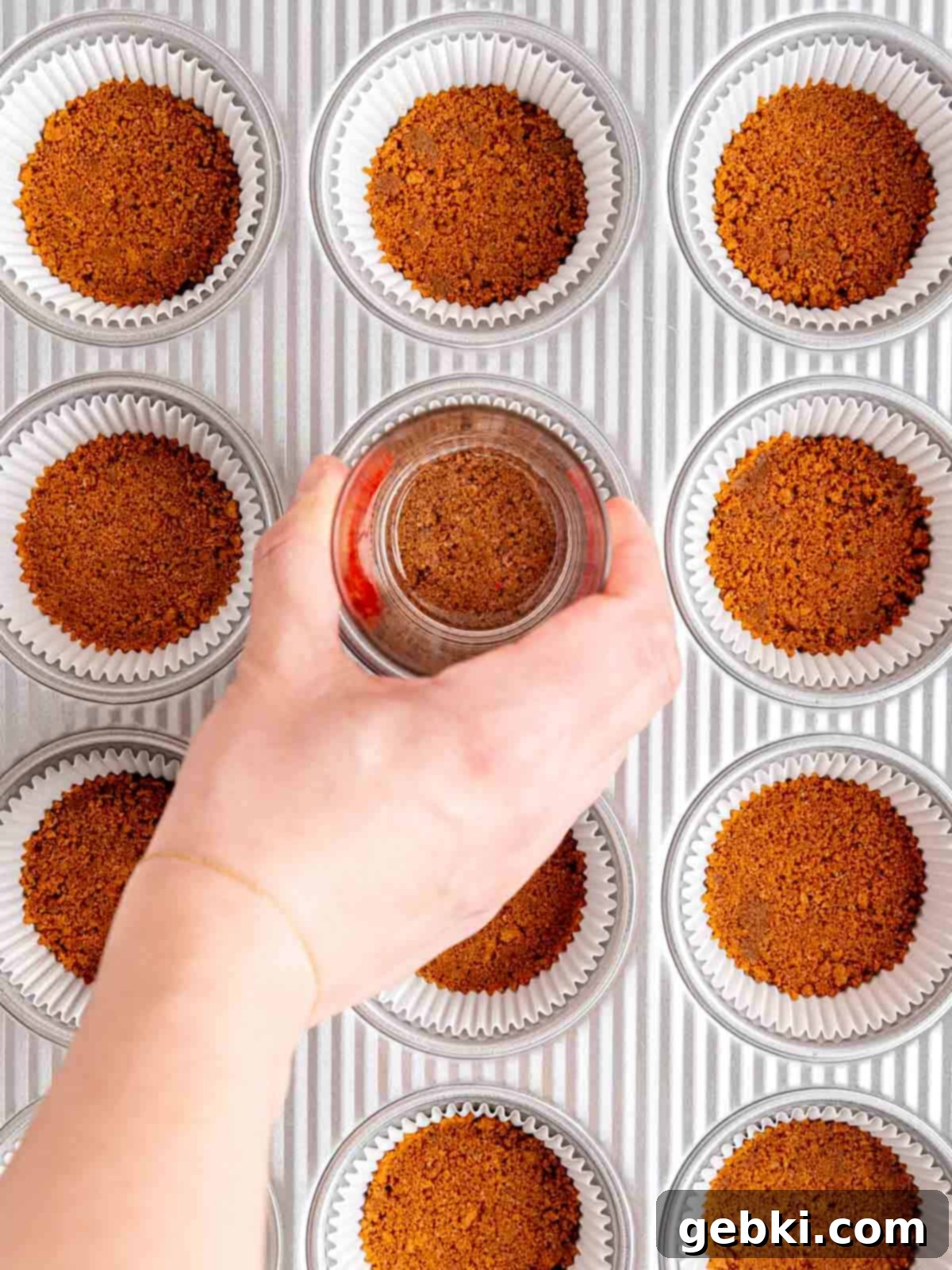 Pressing Biscoff cookie crumbs into cupcake liners using the bottom of a glass.