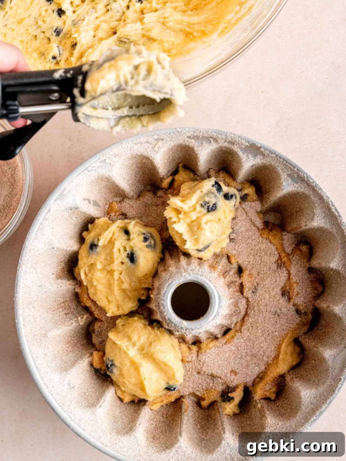Irresistible Blueberry Sour Cream Coffee Cake 8 Filling a cinnamon sugar coated bundt pan with blueberry coffee cake batter.