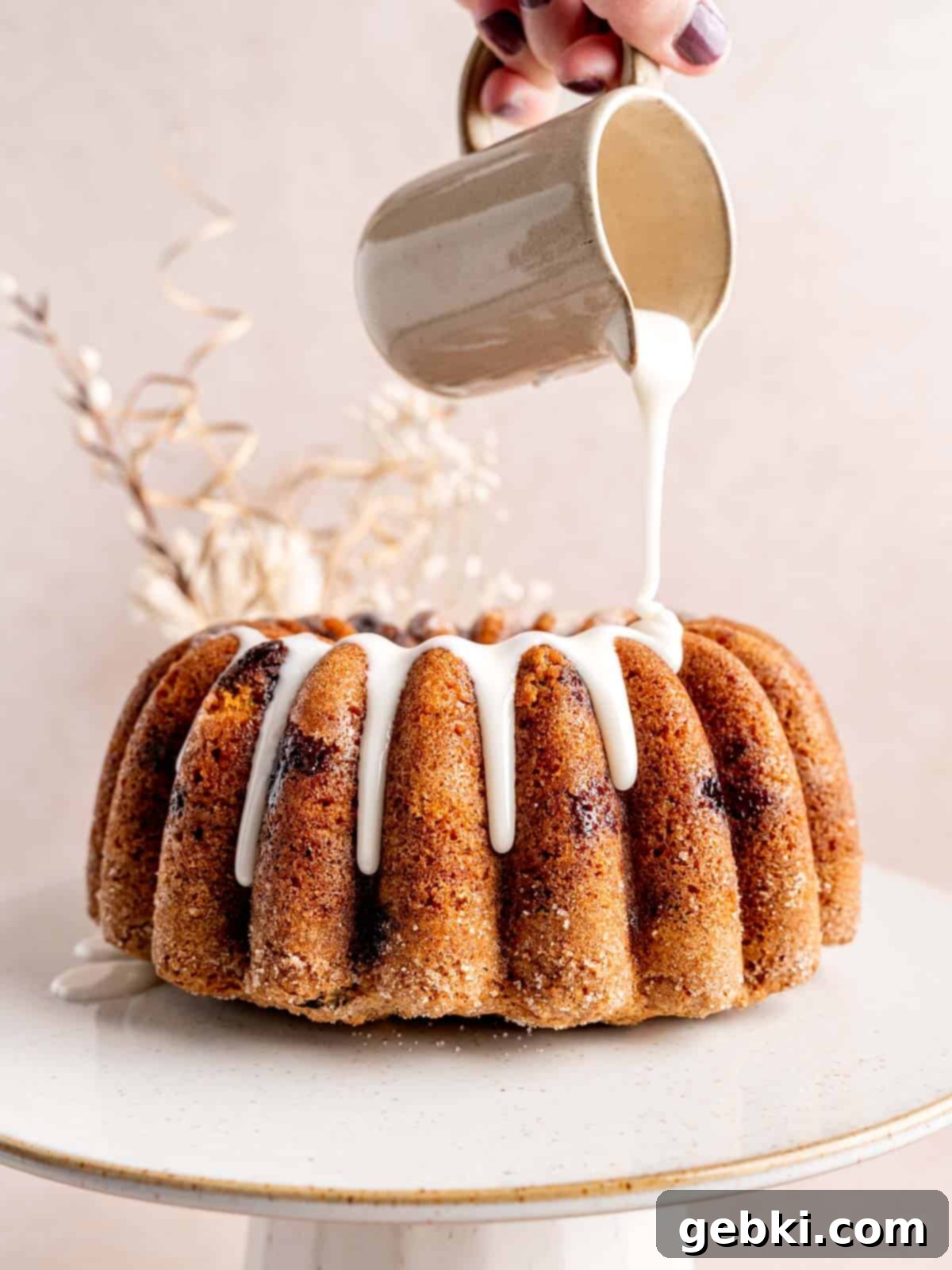 Irresistible Blueberry Sour Cream Coffee Cake 10 Pouring vanilla icing on top of a blueberry coffee cake bundt cake.