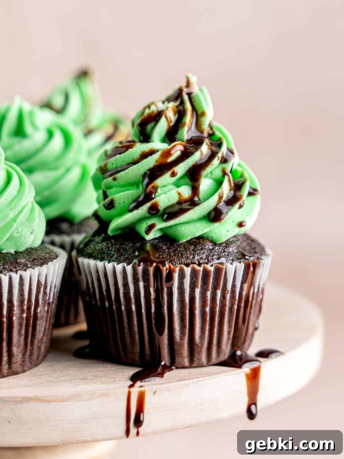 Minty Chocolate Indulgence 2 A chocolate mint cupcake with green mint buttercream frosting and a chocolate drizzle, sitting on a white surface.