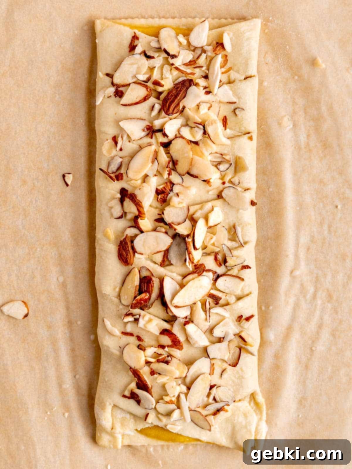 The braided almond danish, brushed with egg wash and topped with an even layer of sliced almonds, ready for baking.