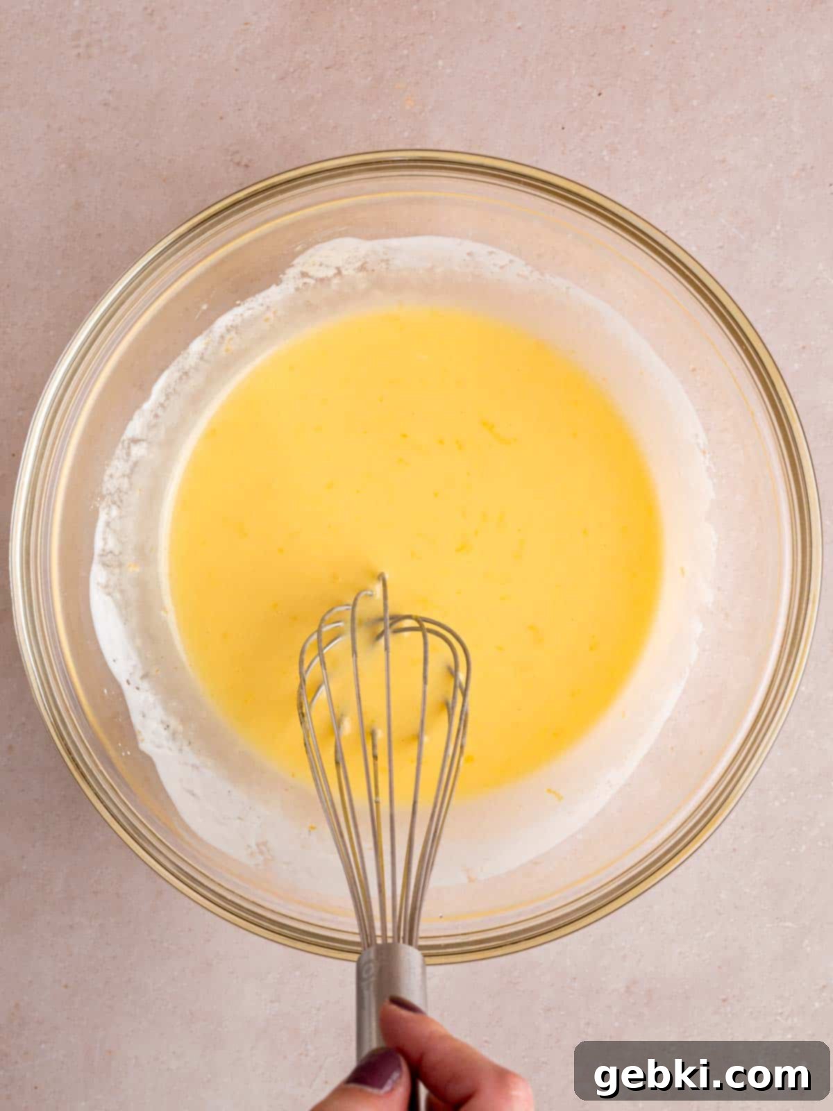 Whisking vegetable oil, sugar, lemon zest, egg, vanilla extract, and lemon kefir in a bowl to create the wet ingredients for the donut batter.