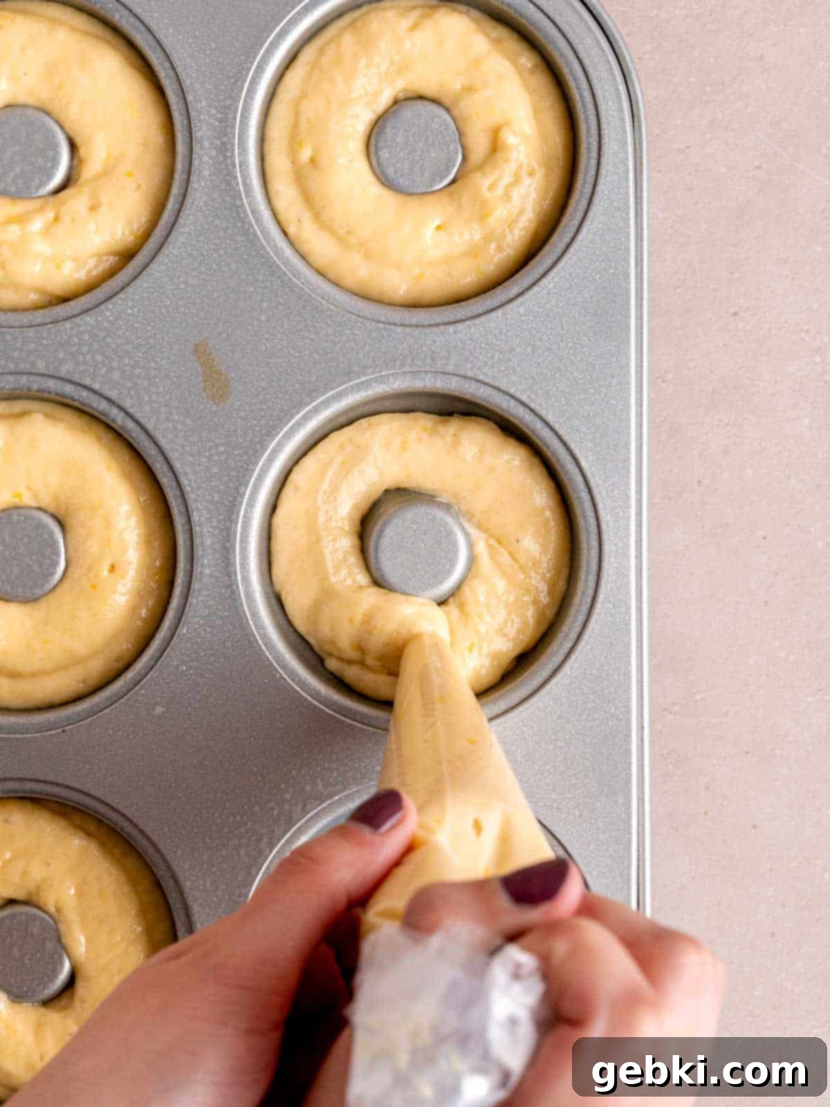Piping lemon cake batter into a greased donut pan, ensuring even filling.