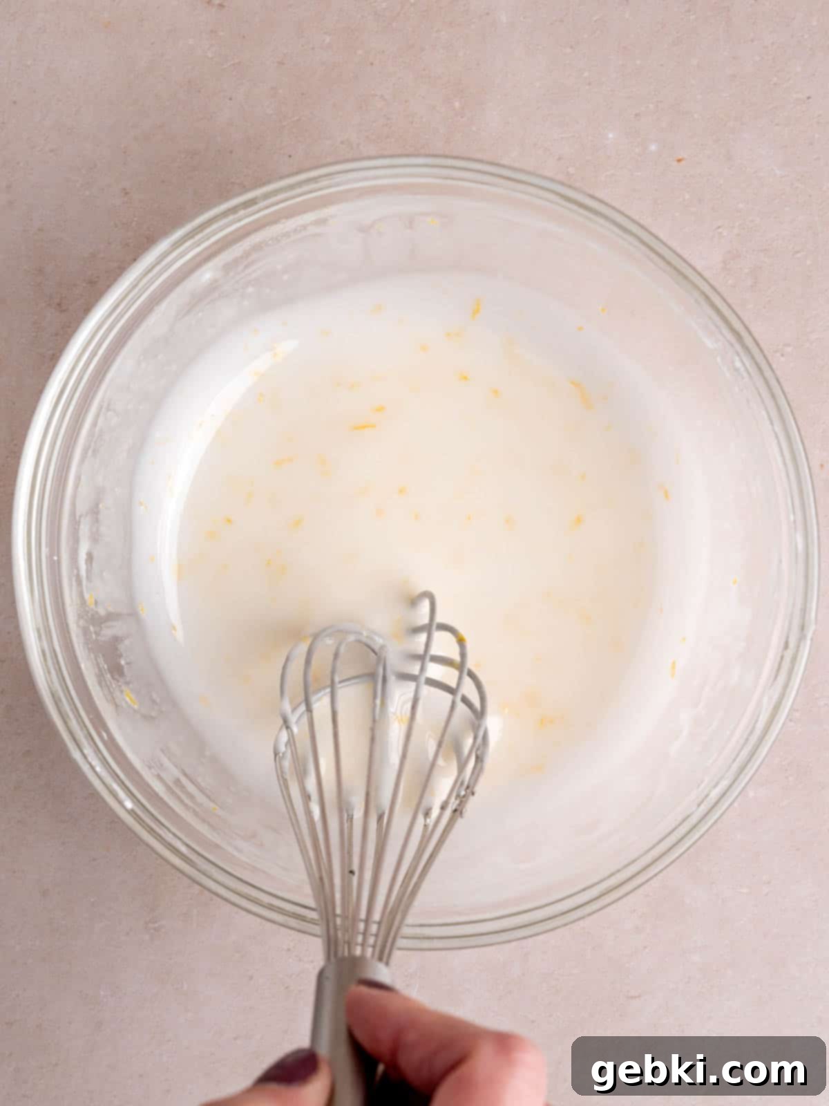 Whisking powdered sugar, lemon juice, lemon zest, and milk in a bowl to create a smooth lemon icing.
