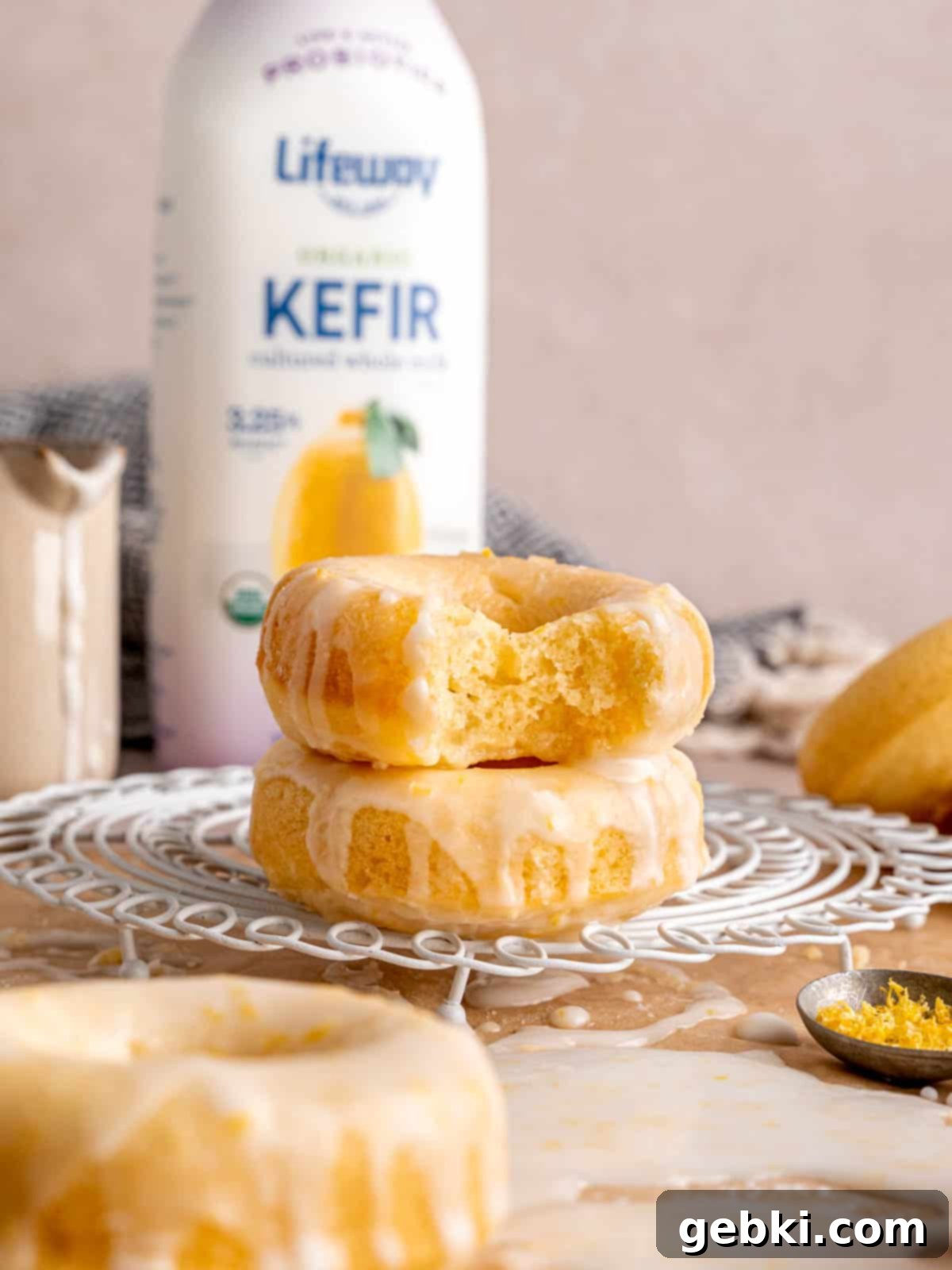 Iced lemon donuts stacked in front of a bottle of Lifeway Lemon Kefir, emphasizing the key ingredient.