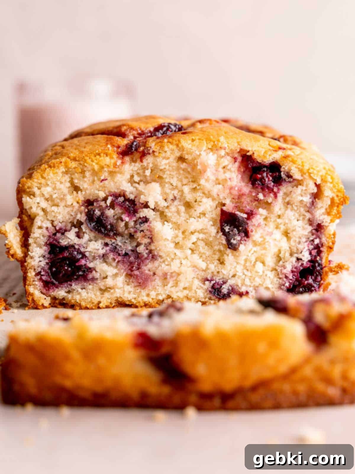 A cherry loaf cake with a slice cut off of the end, showcasing the juicy cherries within.
