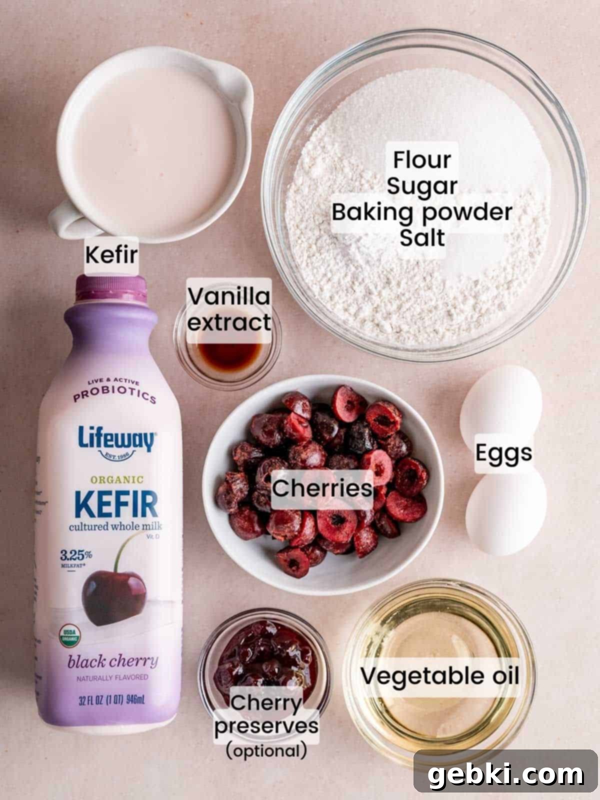 A flat lay photo of the essential ingredients needed to make a cherry loaf cake, including flour, sugar, baking powder, salt, pitted cherries, eggs, Lifeway Black Cherry Kefir, vegetable oil, and vanilla extract.
