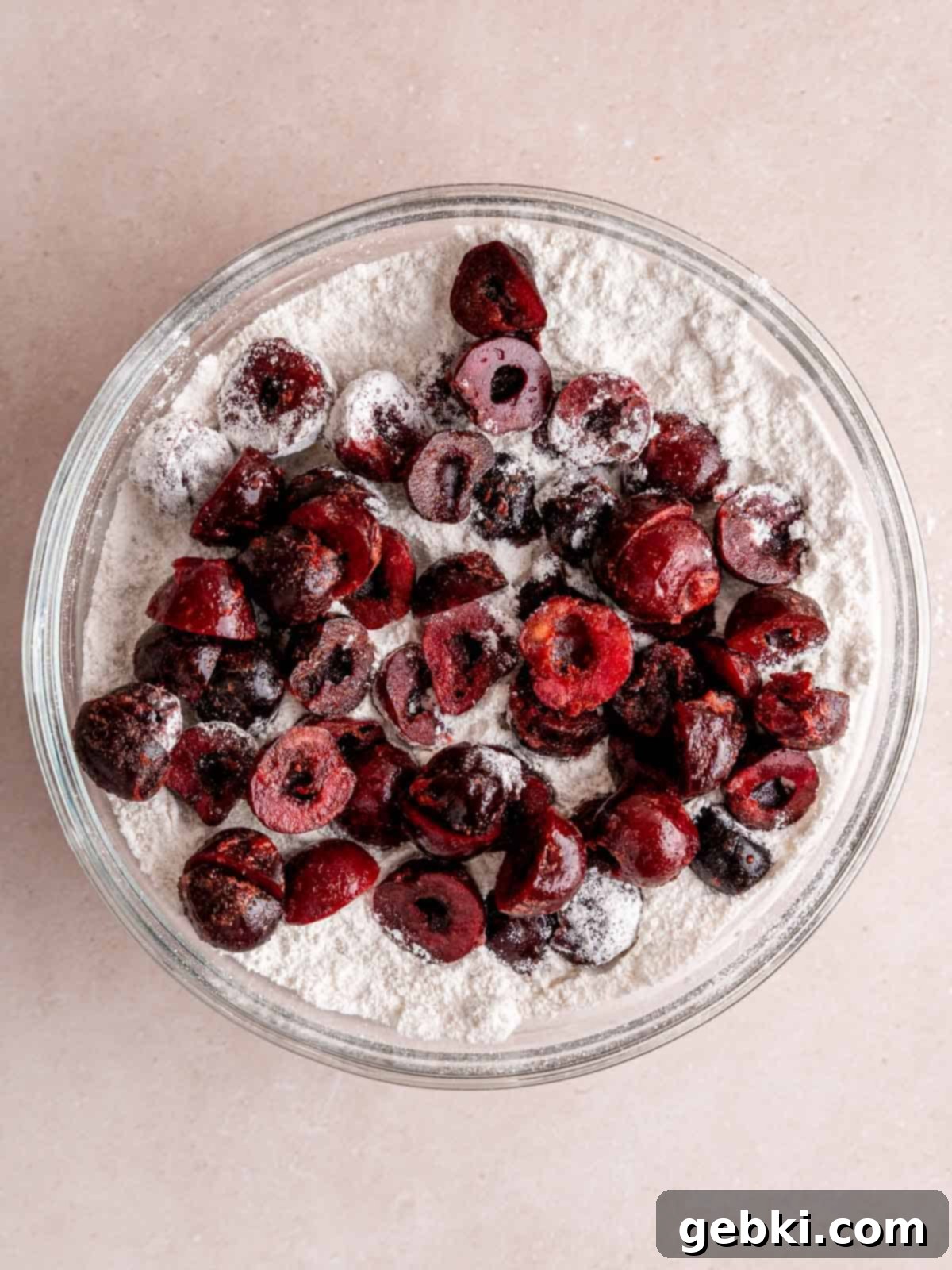 Halved cherries in a bowl of flour mixture, coated lightly to prevent sinking.