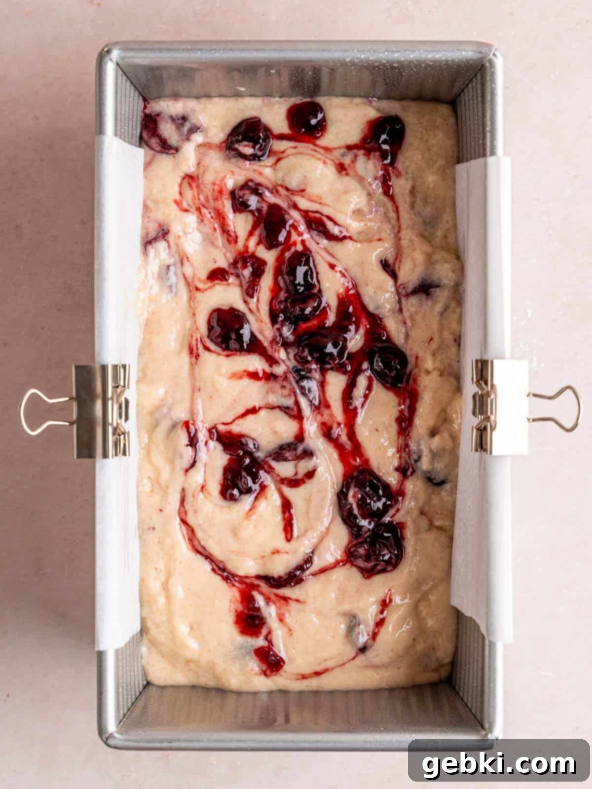 Cherry cake batter in a loaf pan with cherry preserves swirled on top, ready for baking.