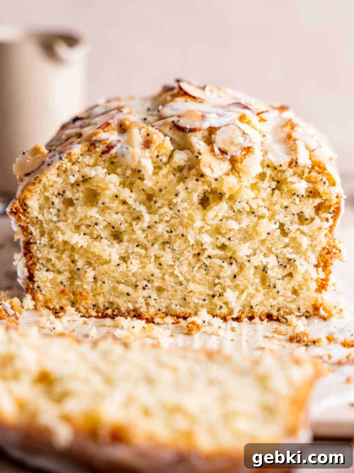 A beautifully baked loaf of moist almond poppy seed cake, generously topped with golden sliced almonds and a glistening almond poppy seed glaze, ready to be sliced and served.