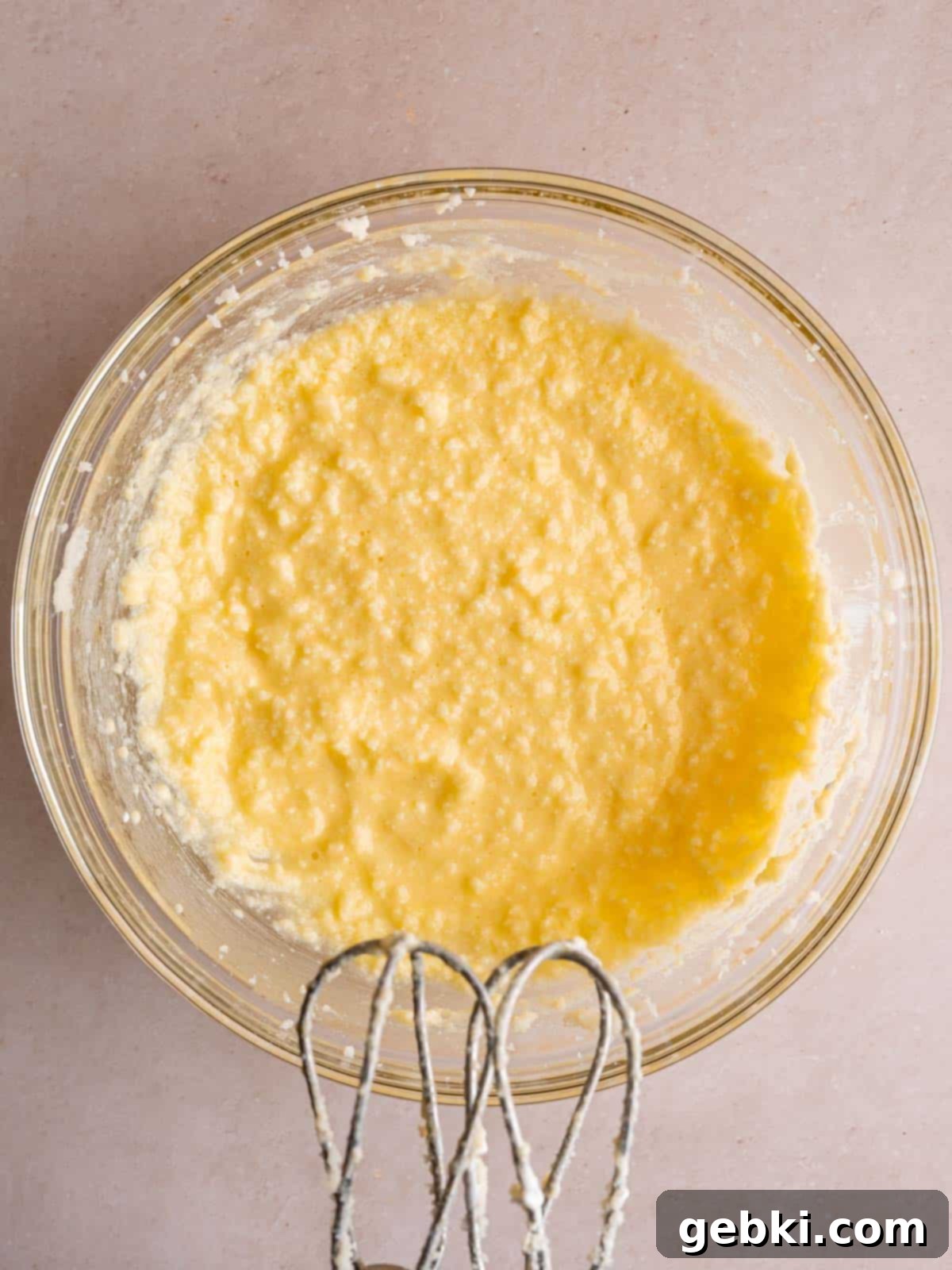 A large bowl filled with creamed butter and granulated sugar, now mixed with eggs, sour cream, and almond extract, creating a smooth, pale yellow wet batter.