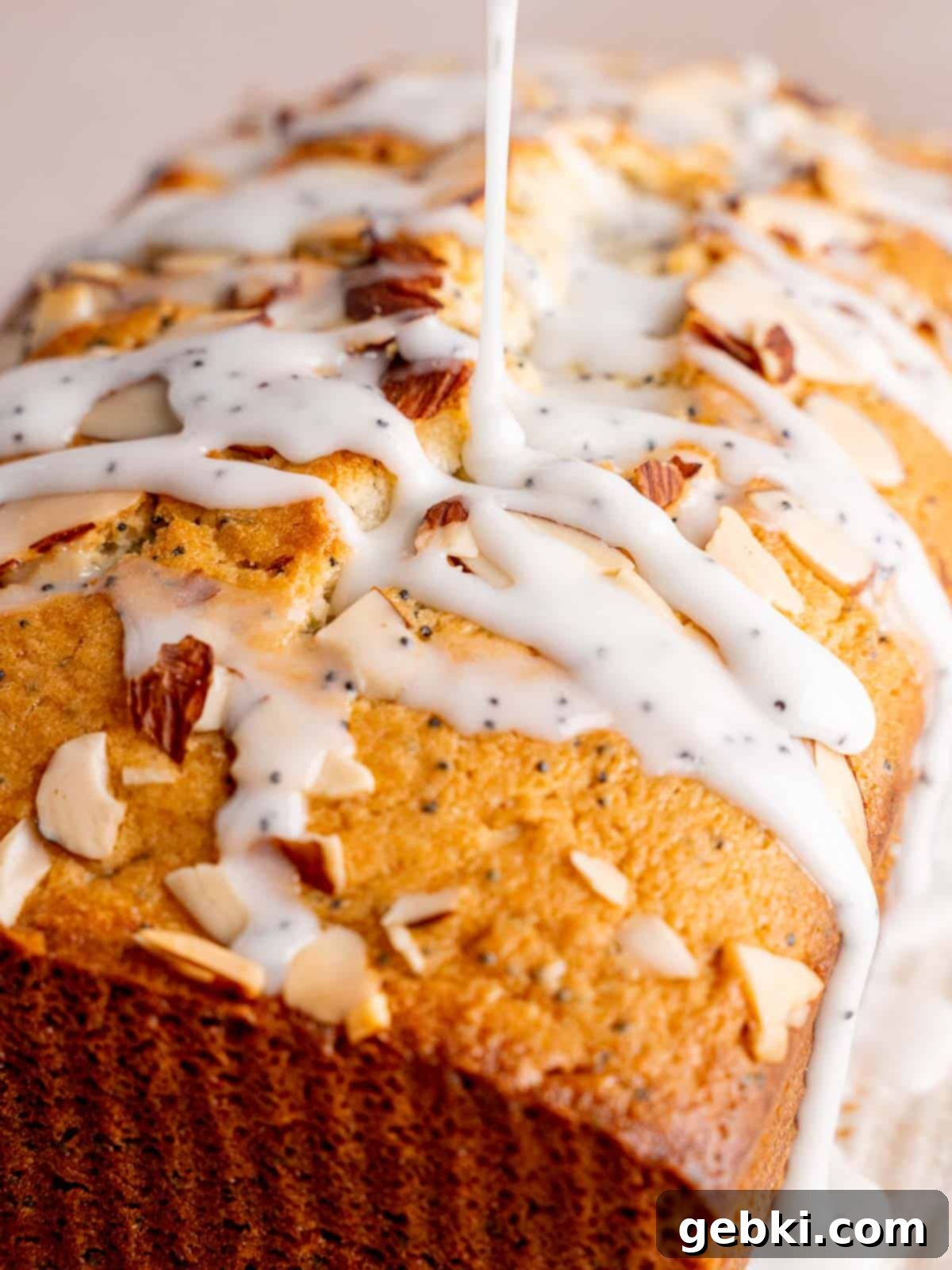 A luscious almond poppy seed glaze being drizzled generously over a perfectly cooled almond poppy seed cake, creating a beautiful finish.