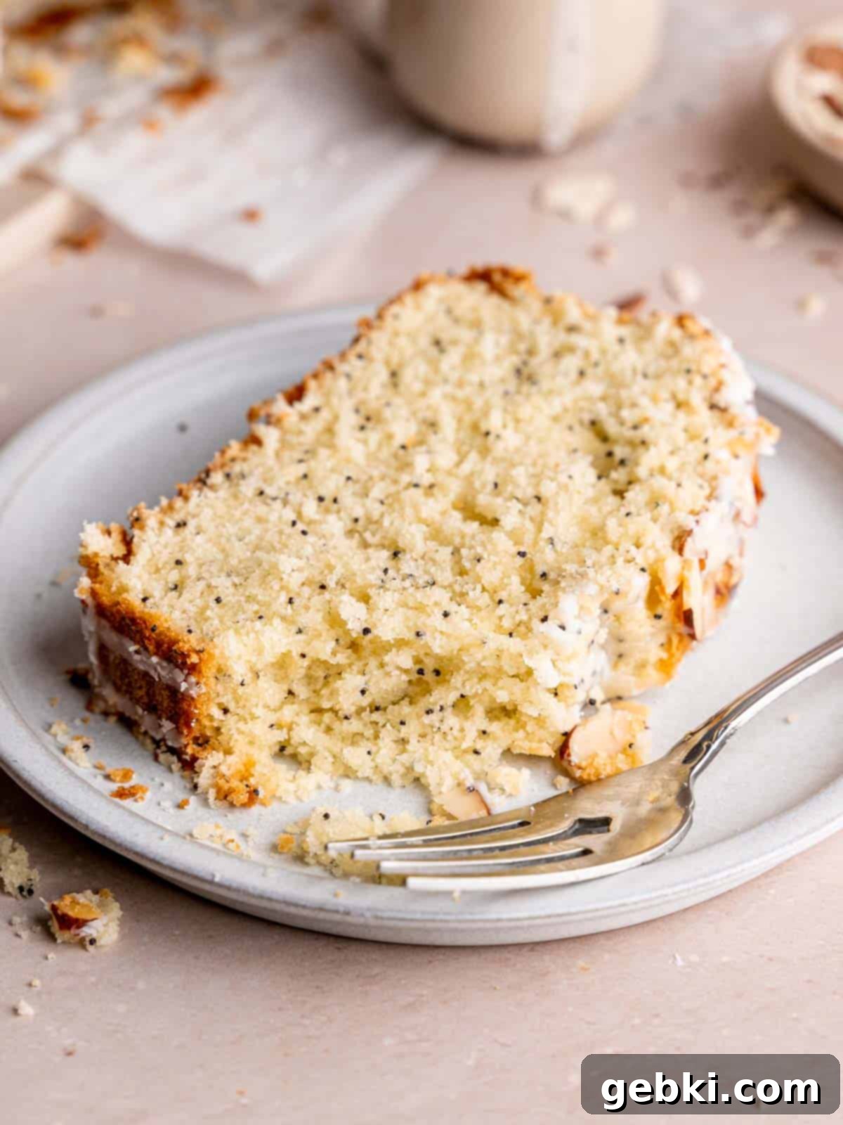 A close-up of a single slice of almond poppy seed cake, showing its moist interior, visible poppy seeds, and crisp toasted almonds, with a bite taken out, highlighting its deliciousness.