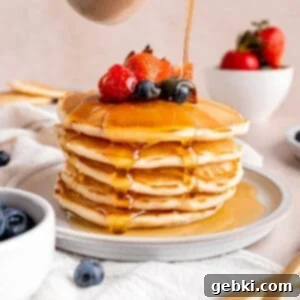 Turn Sourdough Discard Into Fluffy Pancakes 10 Pouring maple syrup over a stack of golden brown, fluffy sourdough discard pancakes, garnished with fresh berries.