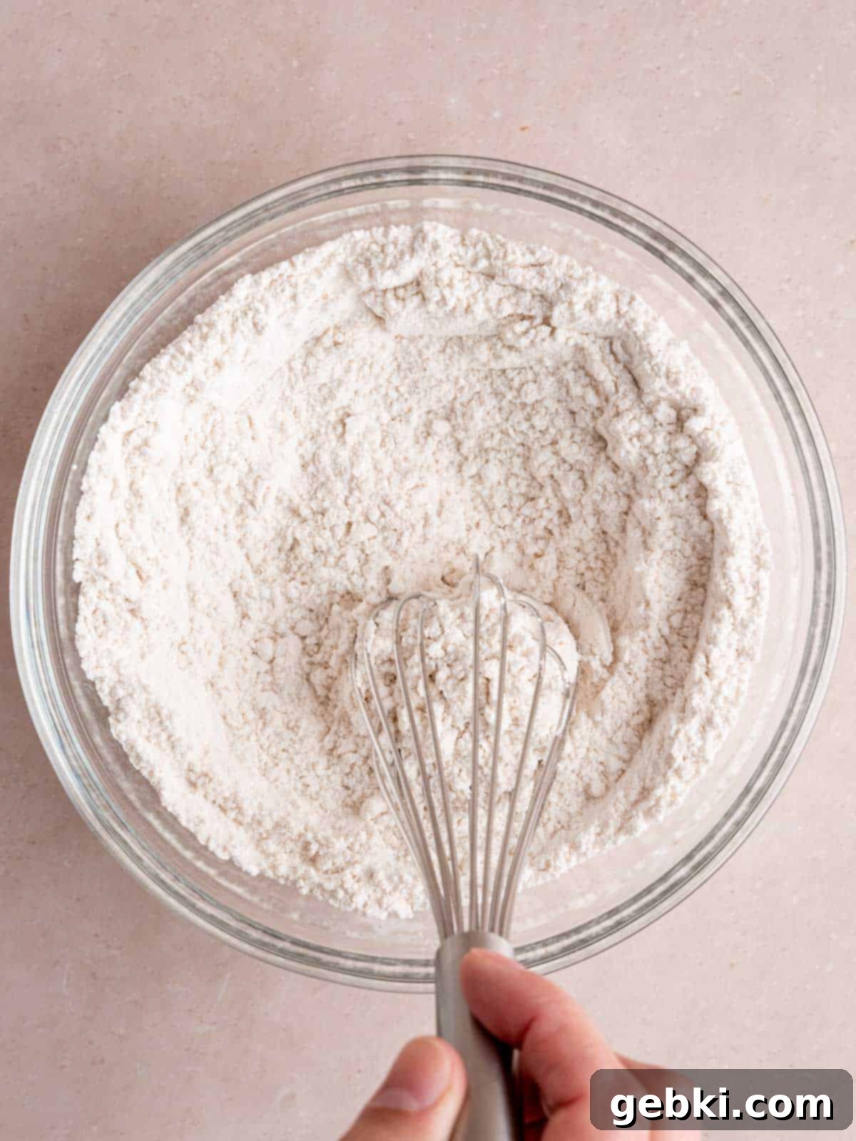 Turn Sourdough Discard Into Fluffy Pancakes 4 A large mixing bowl containing white flour, granulated sugar, baking powder, and salt, being whisked vigorously with a metal whisk to ensure even distribution.