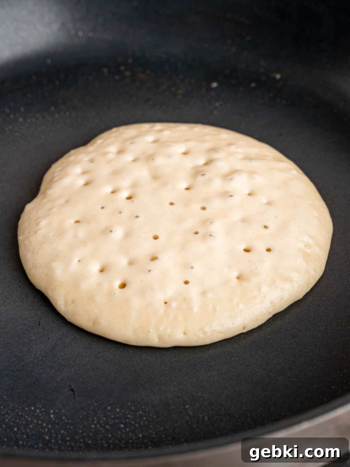 Turn Sourdough Discard Into Fluffy Pancakes 7 Sourdough pancake batter sizzling and cooking on a nonstick skillet, showing numerous small bubbles forming on the surface as it cooks.