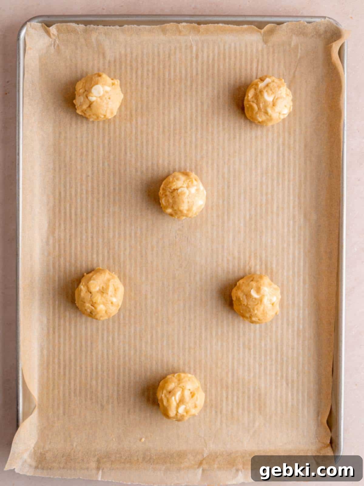 Irresistible White Chocolate Macadamia Nut Cookies 7 Scoops of white chocolate macadamia cookie dough on a baking sheet.