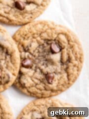 Two chewy sourdough discard chocolate chip cookies, one cut in half to show its soft, gooey interior.