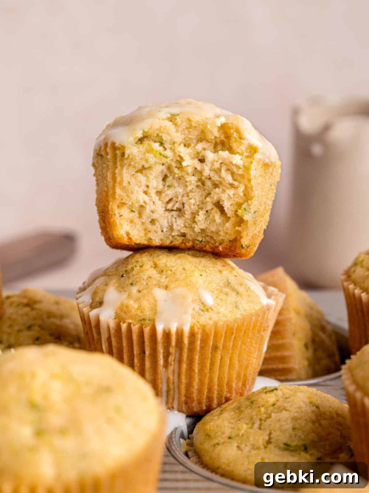 A stack of lemon zucchini muffins with lemon icing, garnished with lemon zest.