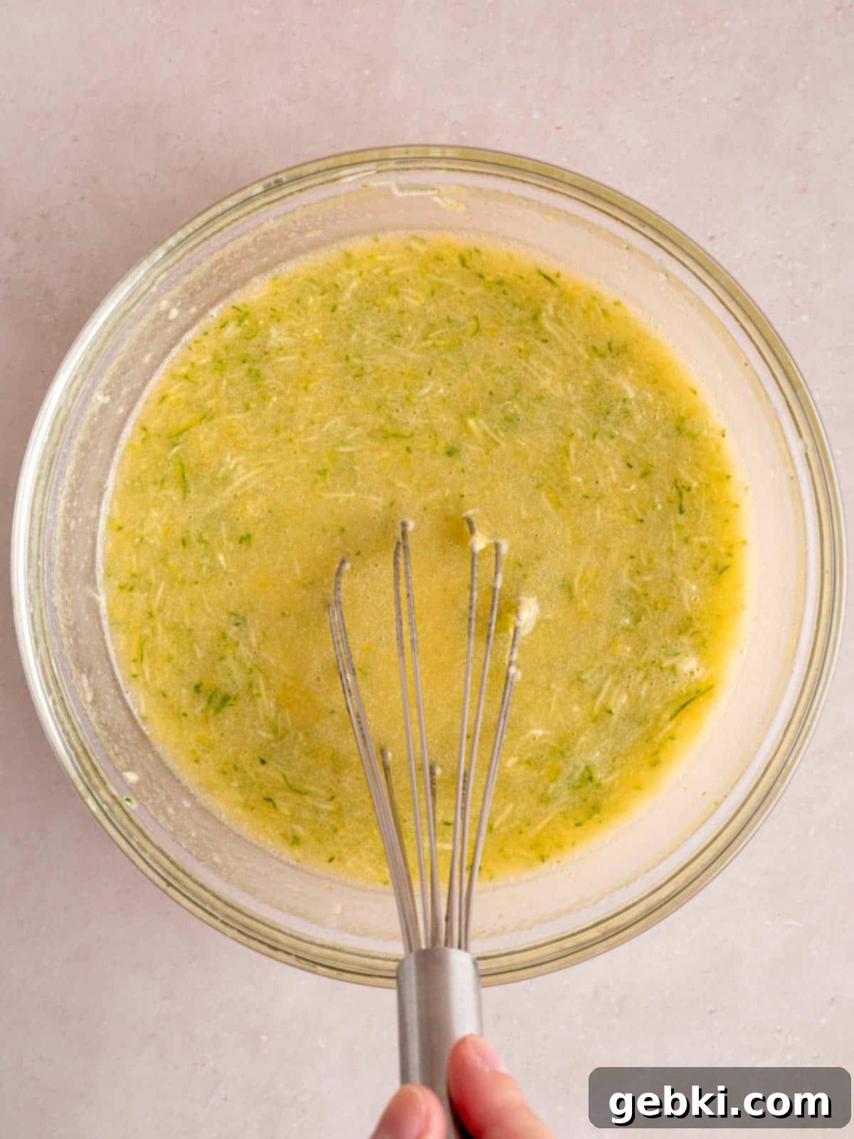 Whisking vegetable oil, sugar, lemon zest, eggs, lemon kefir, vanilla extract, and shredded zucchini in a separate bowl.