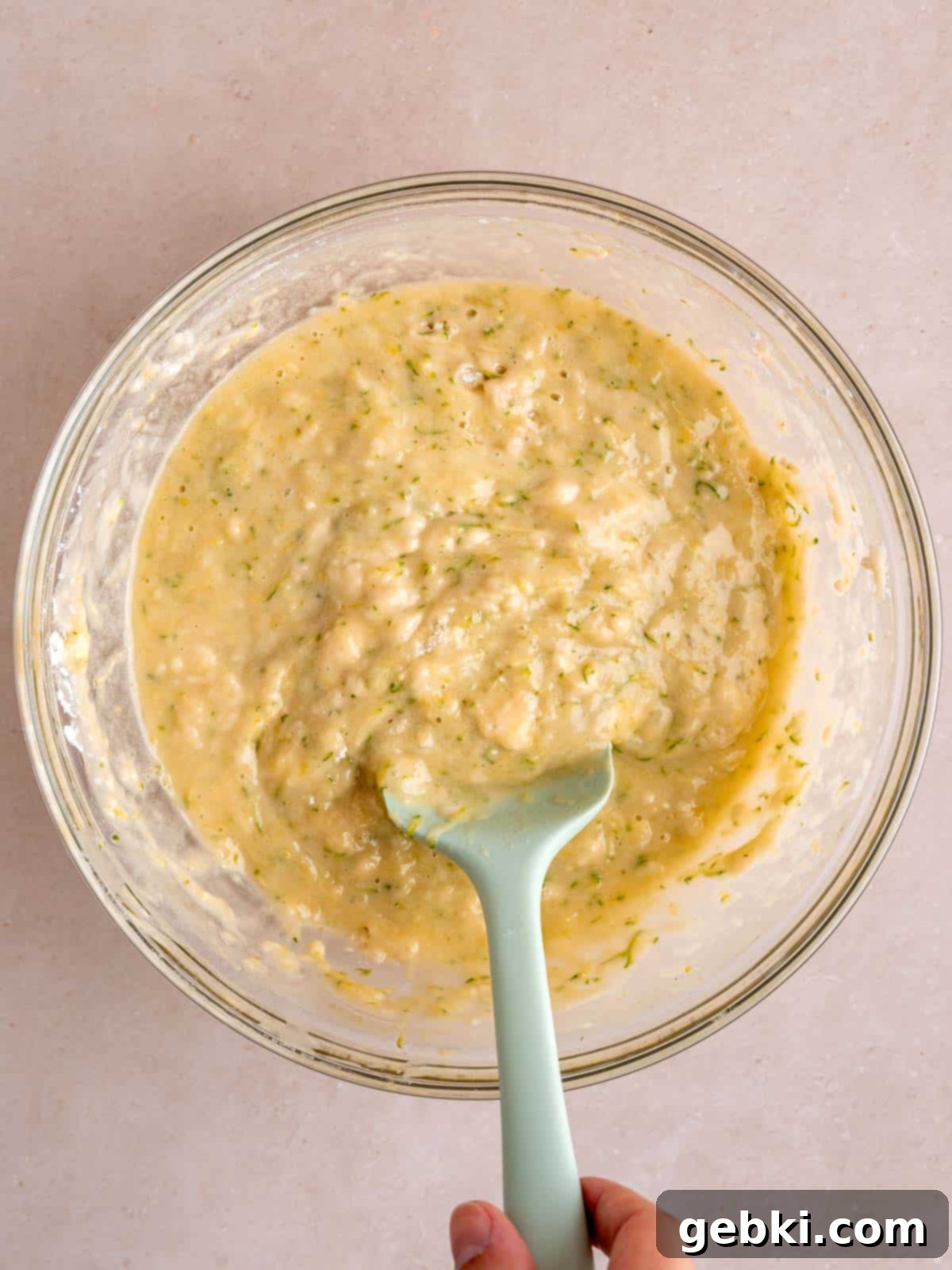 Lemon zucchini muffin batter in a bowl, showing a smooth but not overmixed consistency, with a spatula.
