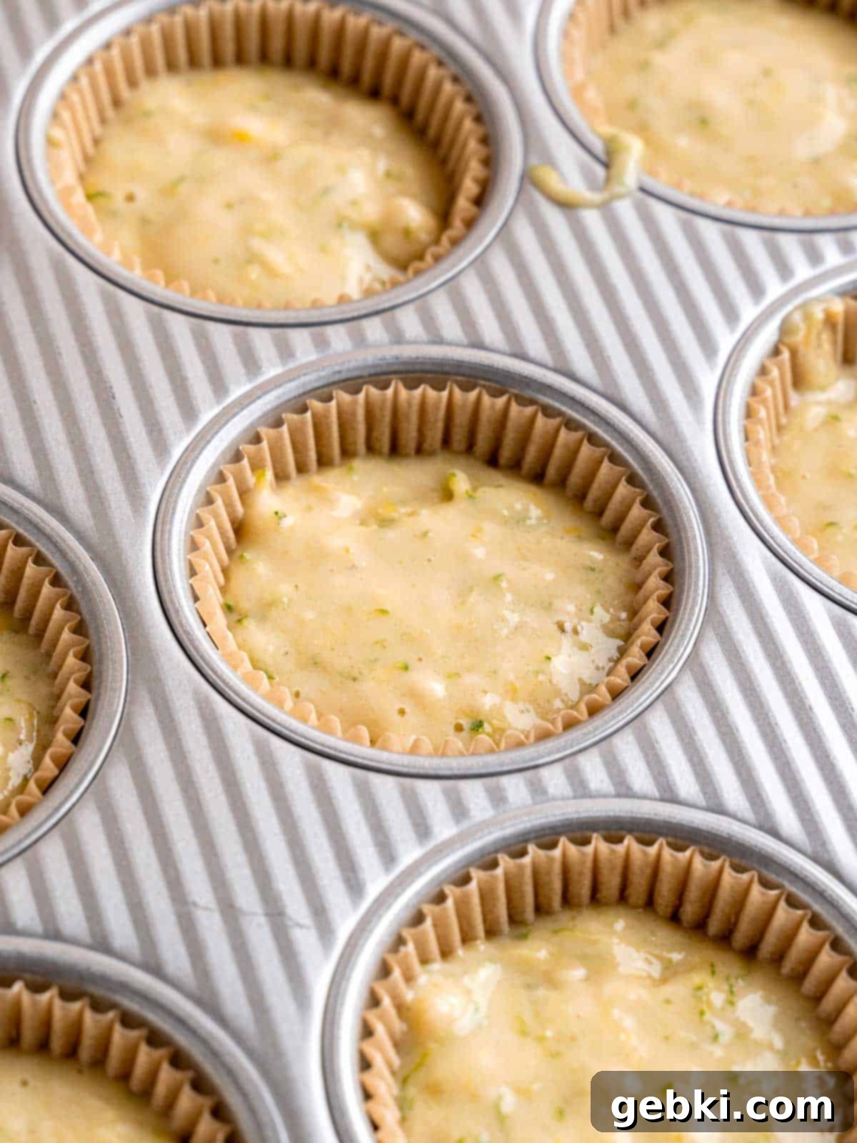 A muffin pan filled with liners, each containing the prepared lemon zucchini batter, ready for baking.
