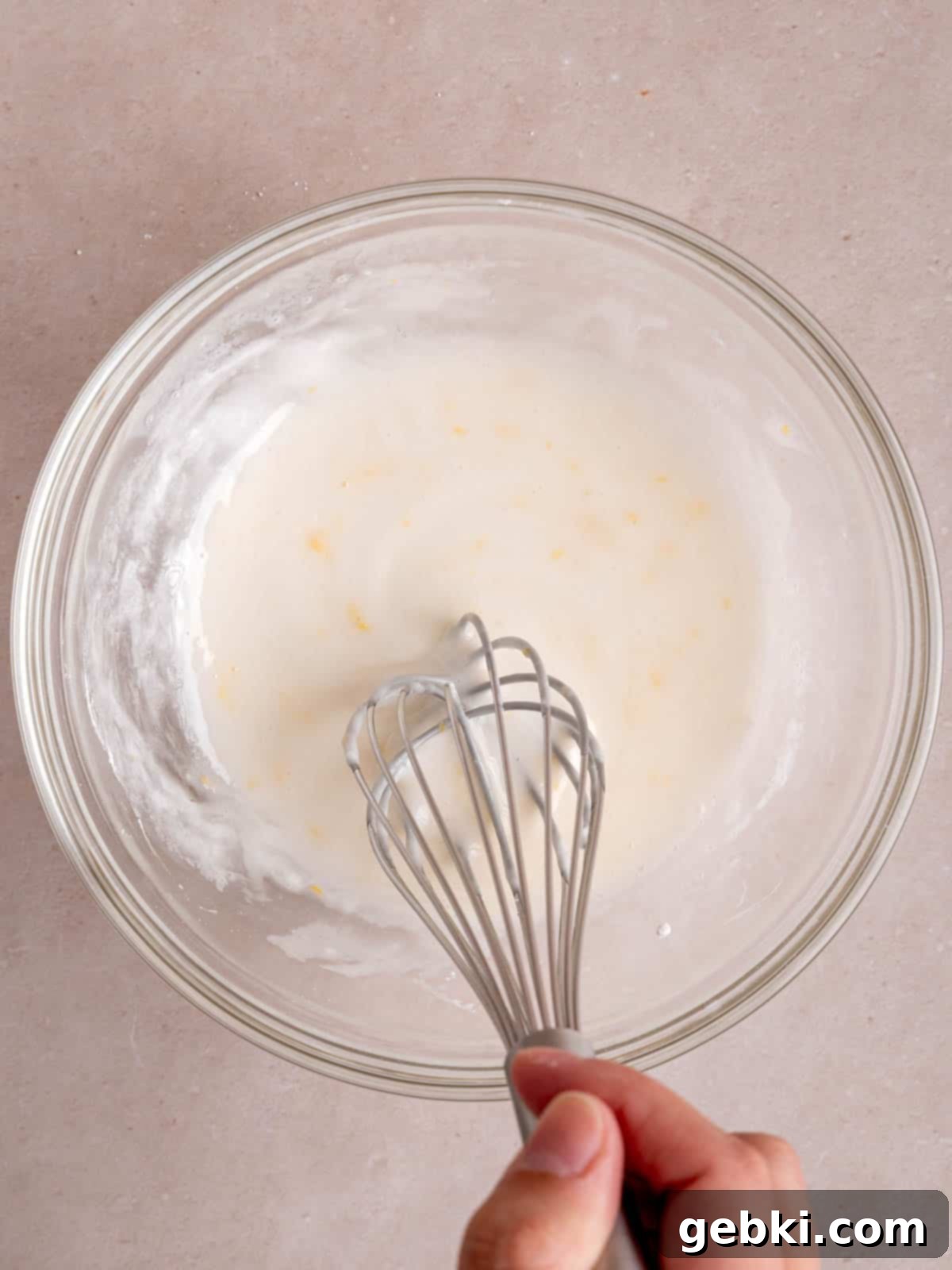 Whisking powdered sugar, milk, lemon zest, and lemon juice in a bowl to create the lemon icing.