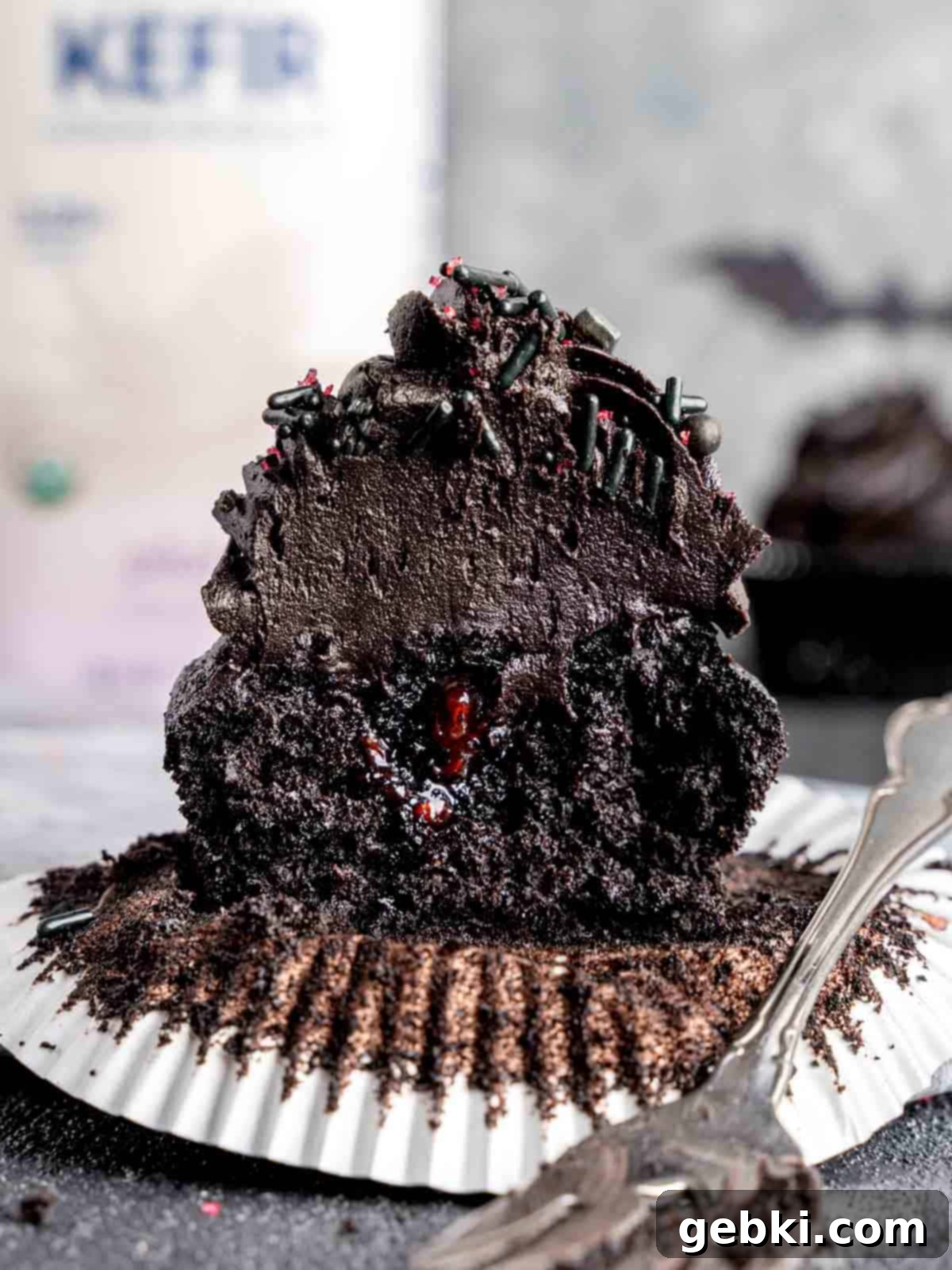 A black cocoa cupcake cut in half showing the raspberry filling.