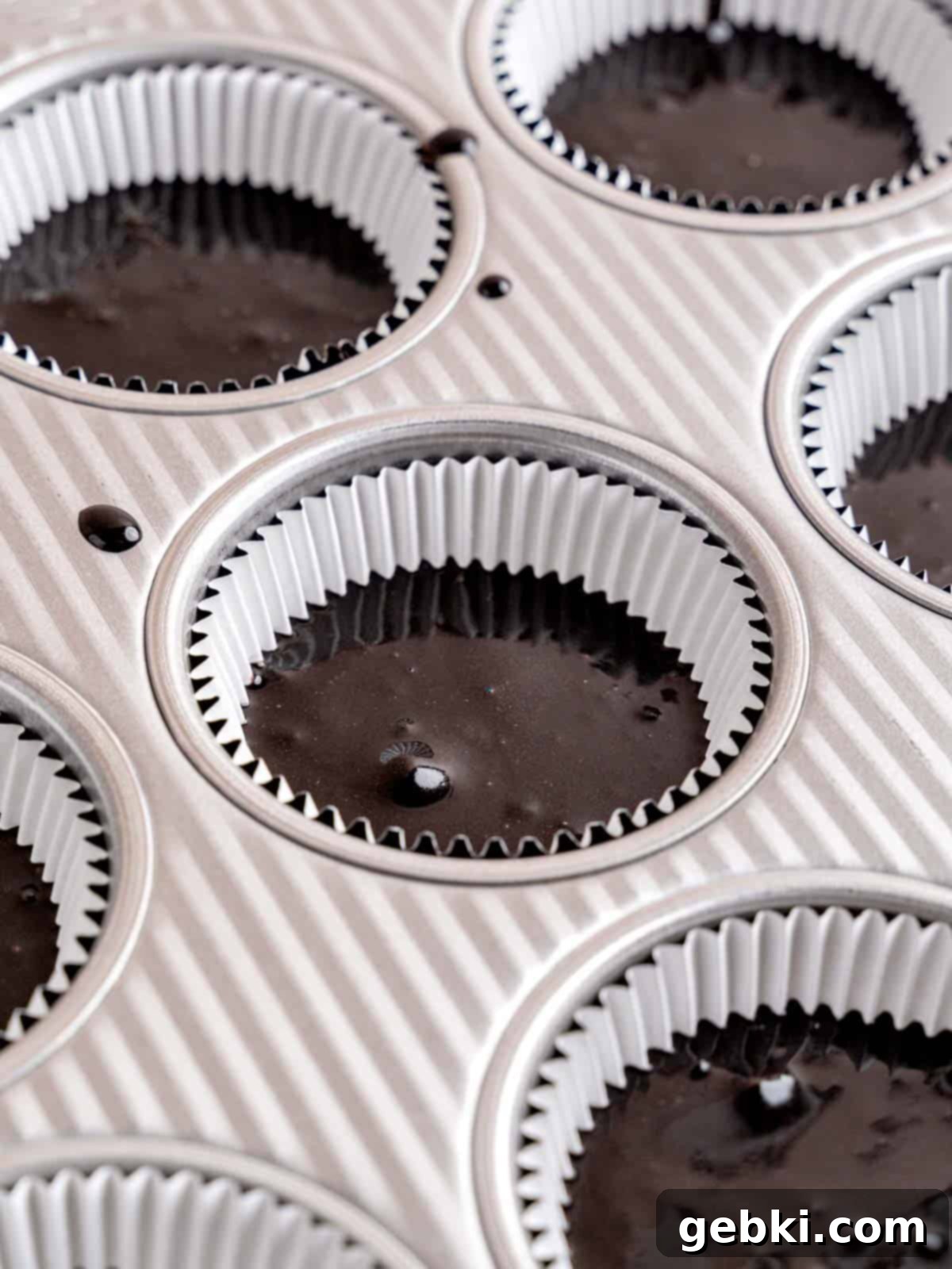 A cupcake pan filled with black cupcake batter.