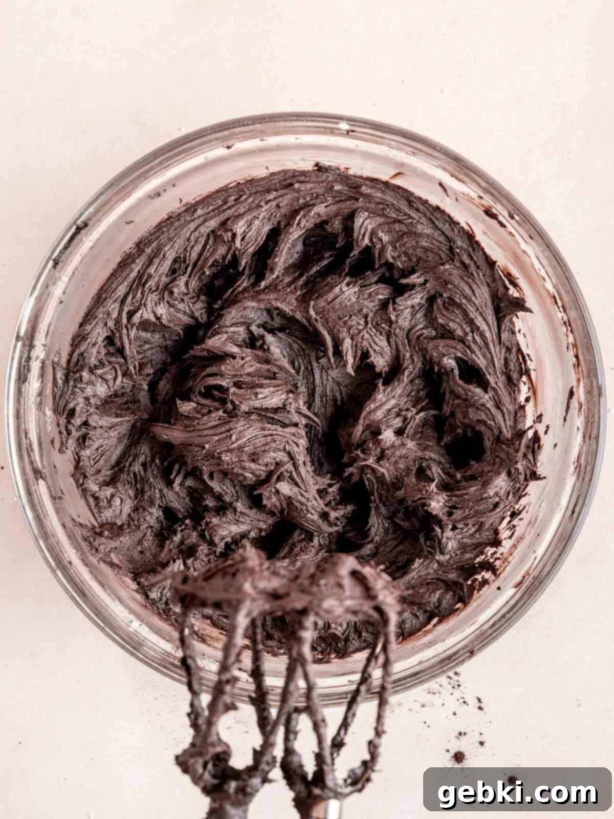 Black buttercream mixed in a bowl with a hand mixer.