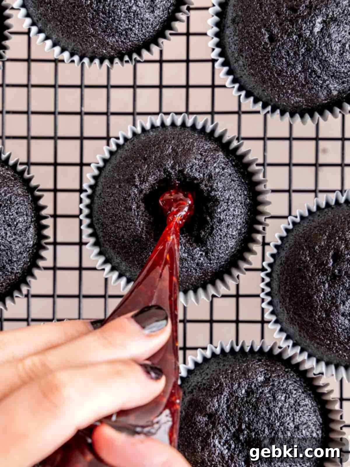 Filling the center of a cupcake with raspberry preserves.